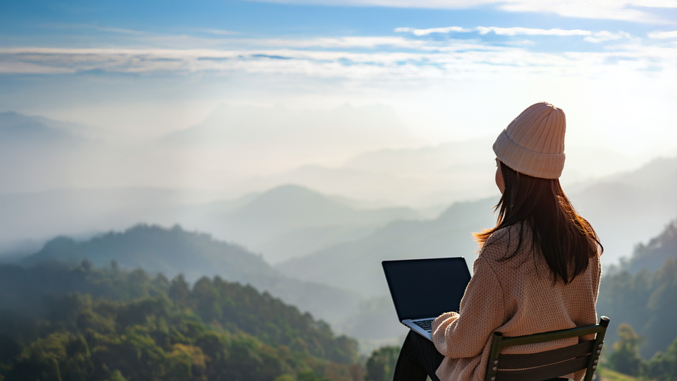 En kvinna sitter och arbetar med en utsikt av öppna landskap och gröna kullar. Hon arbetar "hemifrån".