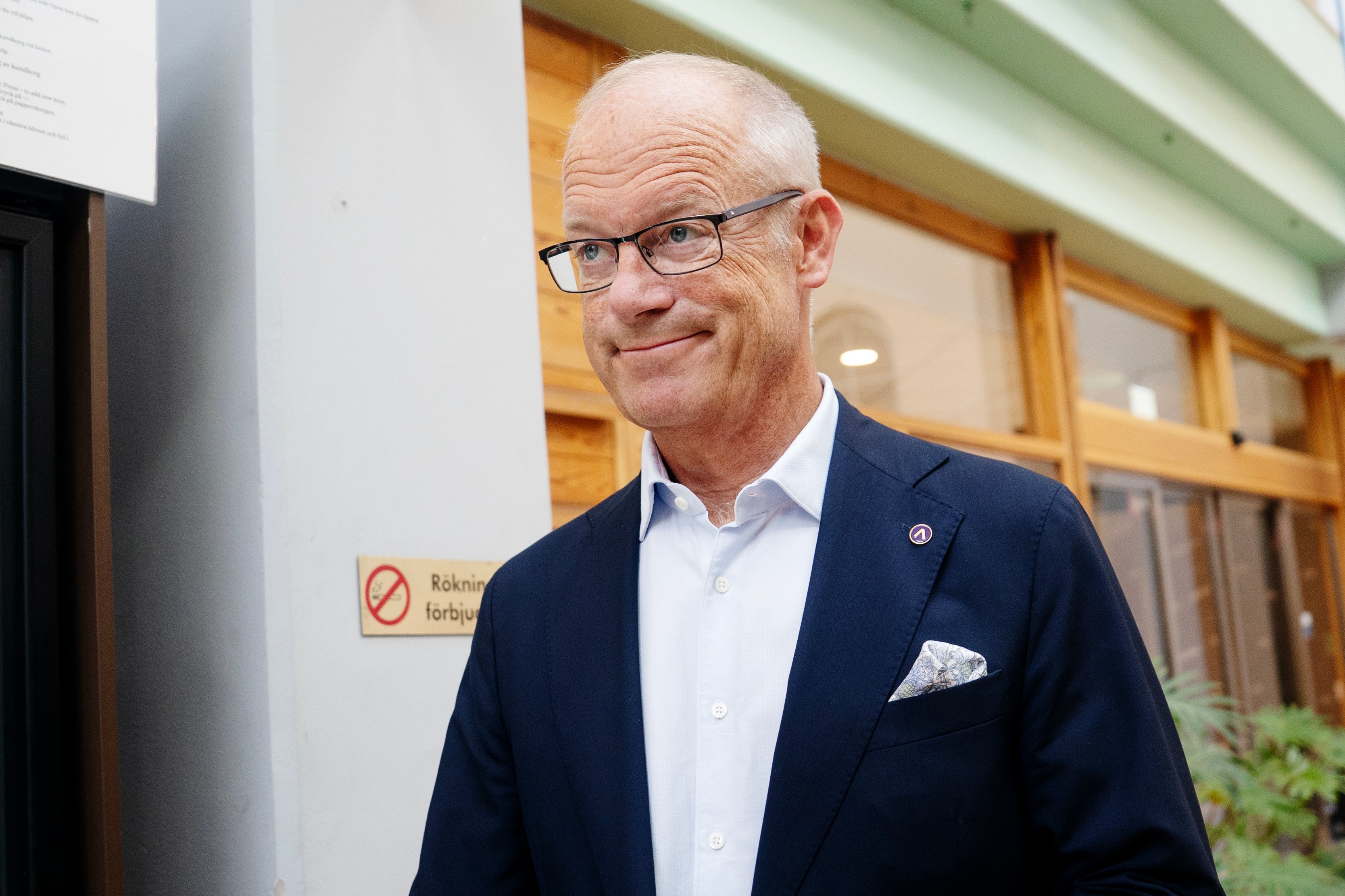 Porträtt av en man med glasögon som bär mörk blazer och ljus skjorta. Han står inomhus framför träfönster och ler mot kameran.