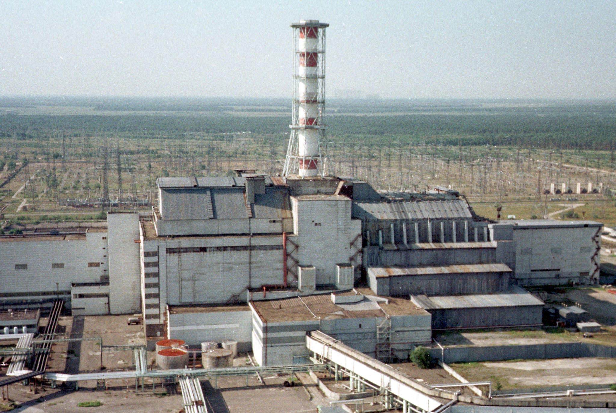 Luftfoto av Tjernobyl-kärnkraftverket med reaktorbyggnaden och kyltornet omgivet av platt, gles terräng.