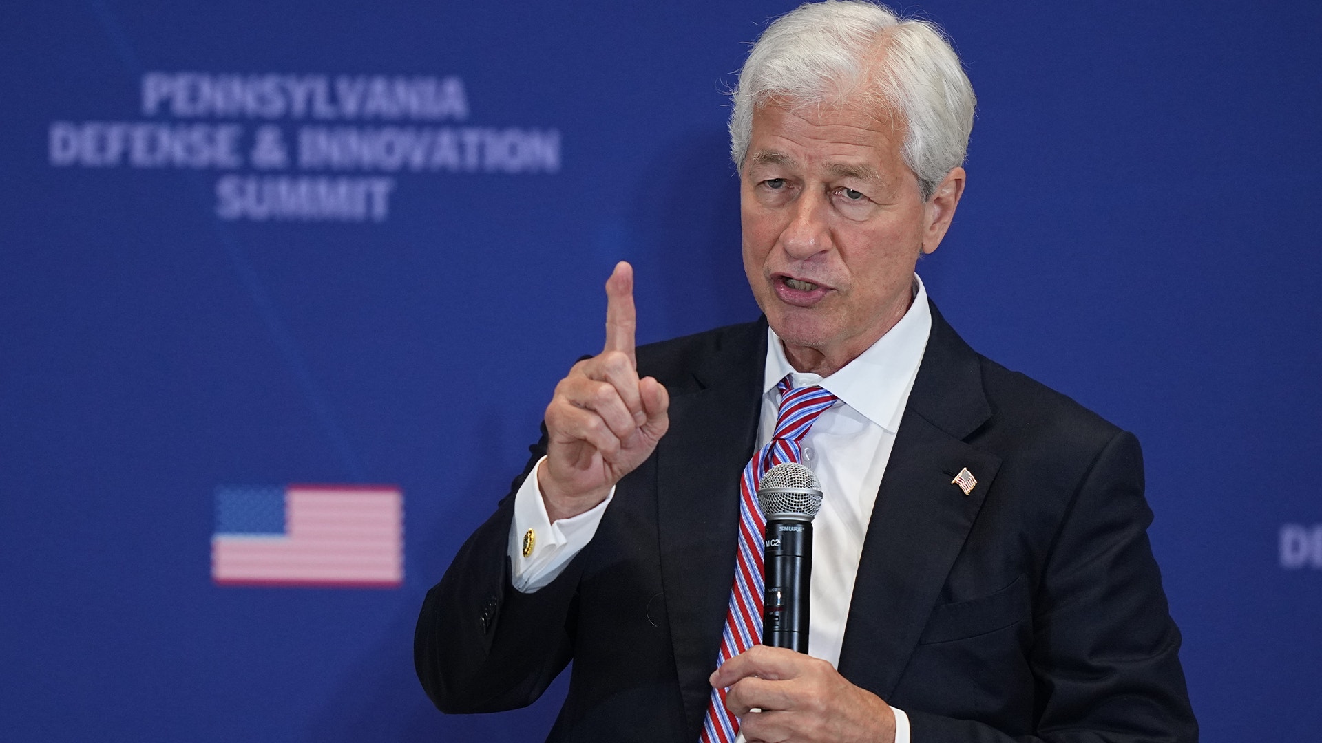 Man i kostym talar vid mikrofon framför blå bakgrund med Pennsylvania Defense & Innovation Summit-logotyp.