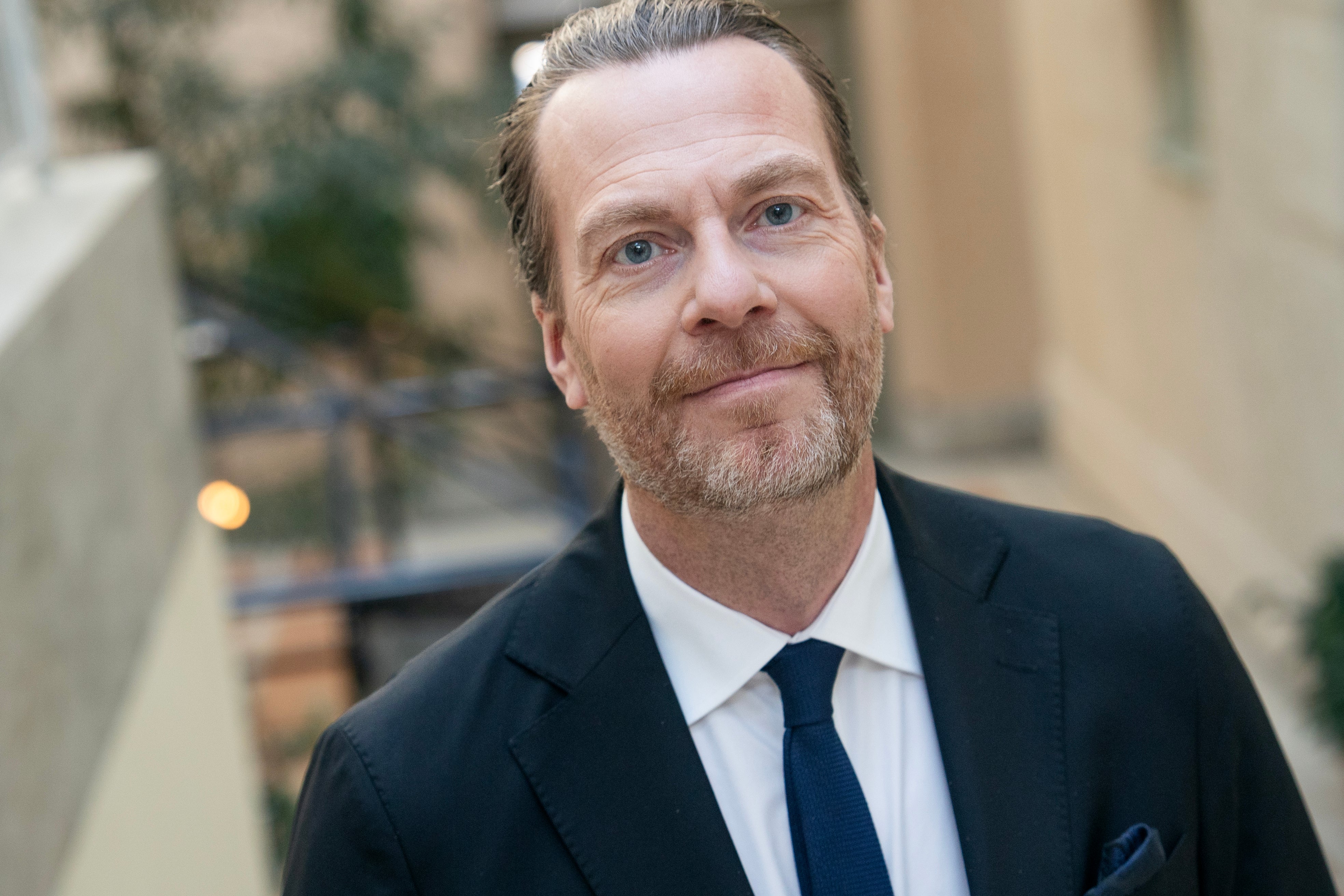 Porträtt av en man i kostym och slips mot en stadsbyggnad i bakgrunden