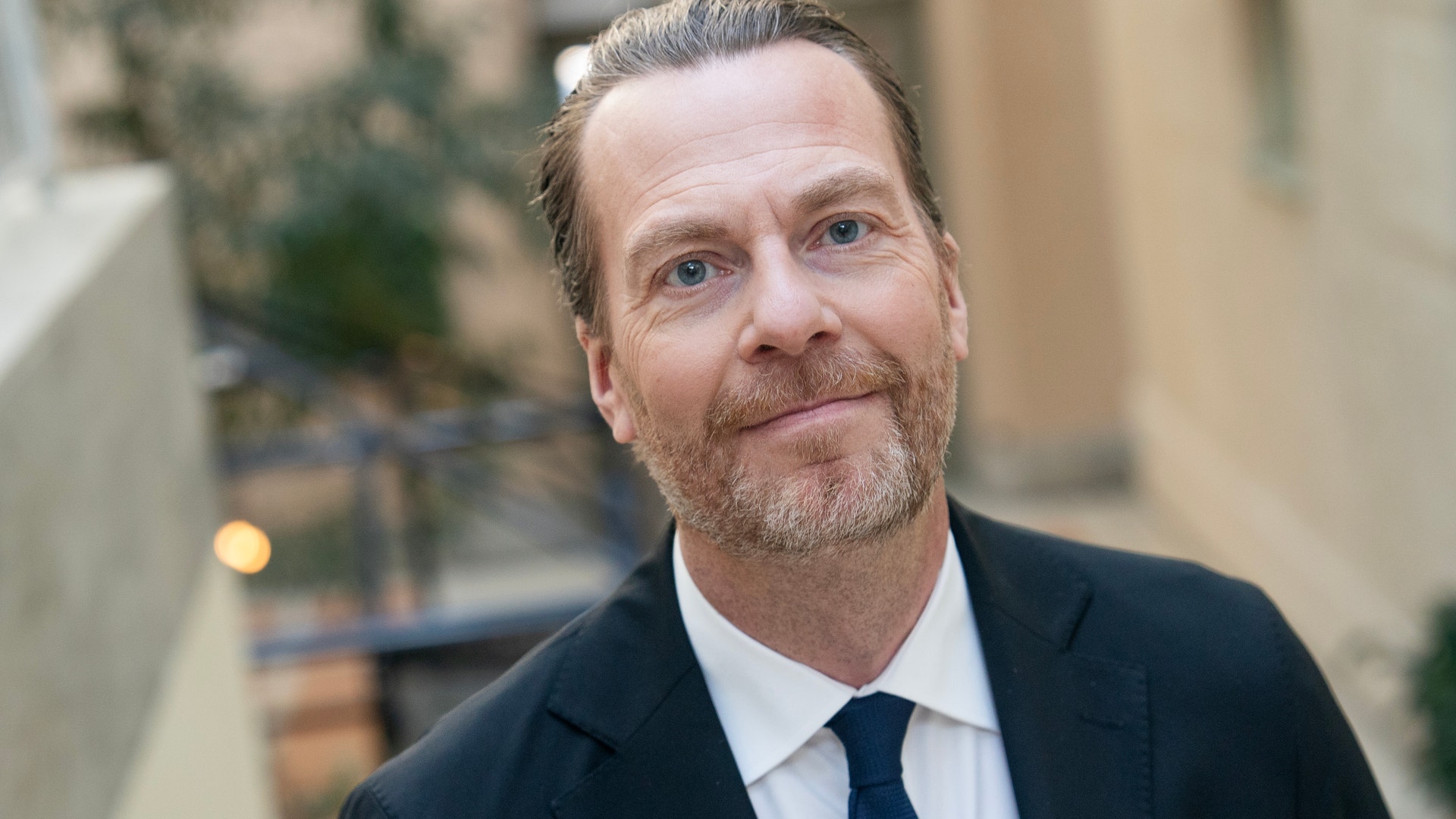 Porträtt av en man i kostym och slips mot en stadsbyggnad i bakgrunden