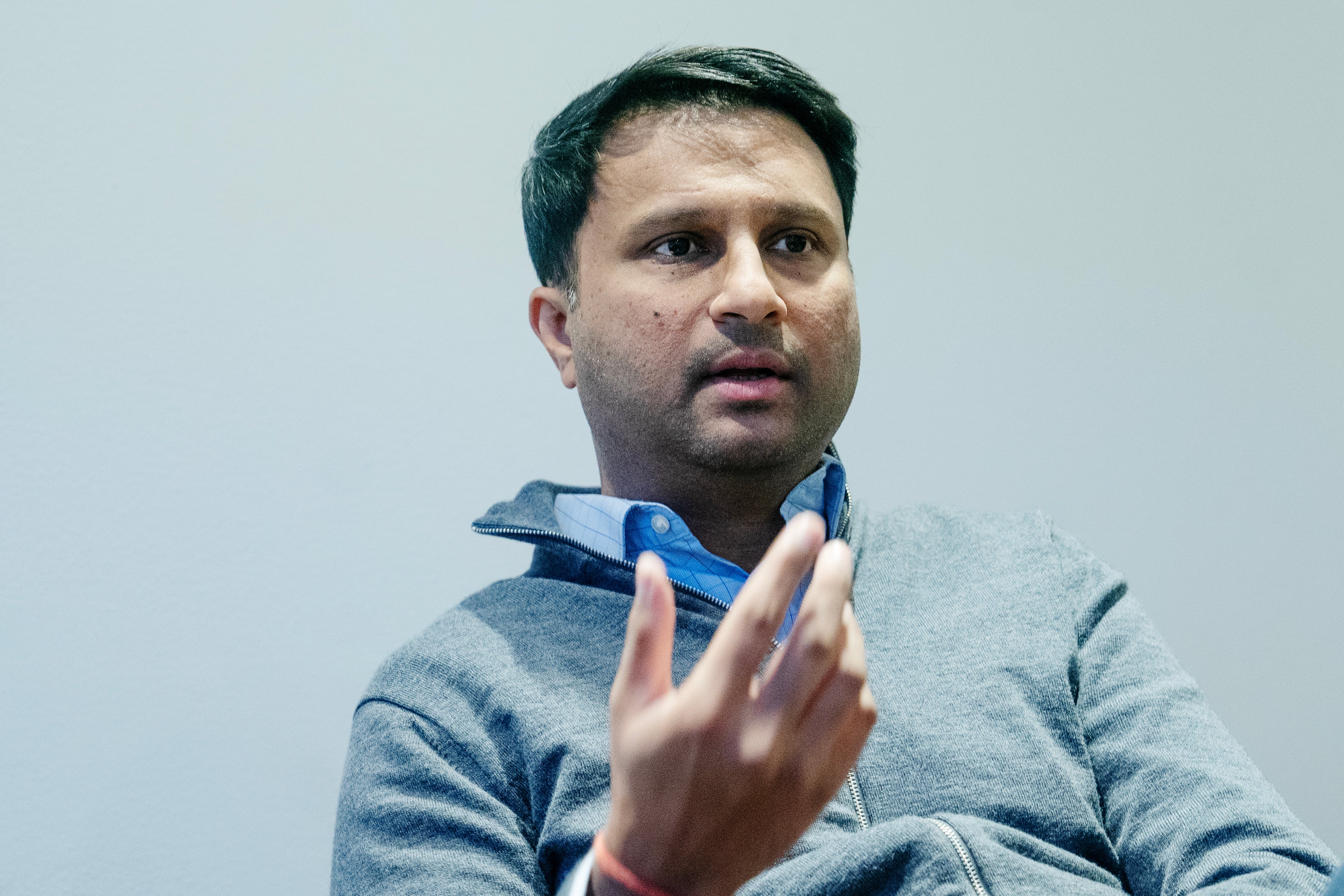 Porträtt av Rishit Jhunjhunwala, en man i grå tröja med blå halsduk, som gestikulerar medan han talar mot en ljus bakgrund.