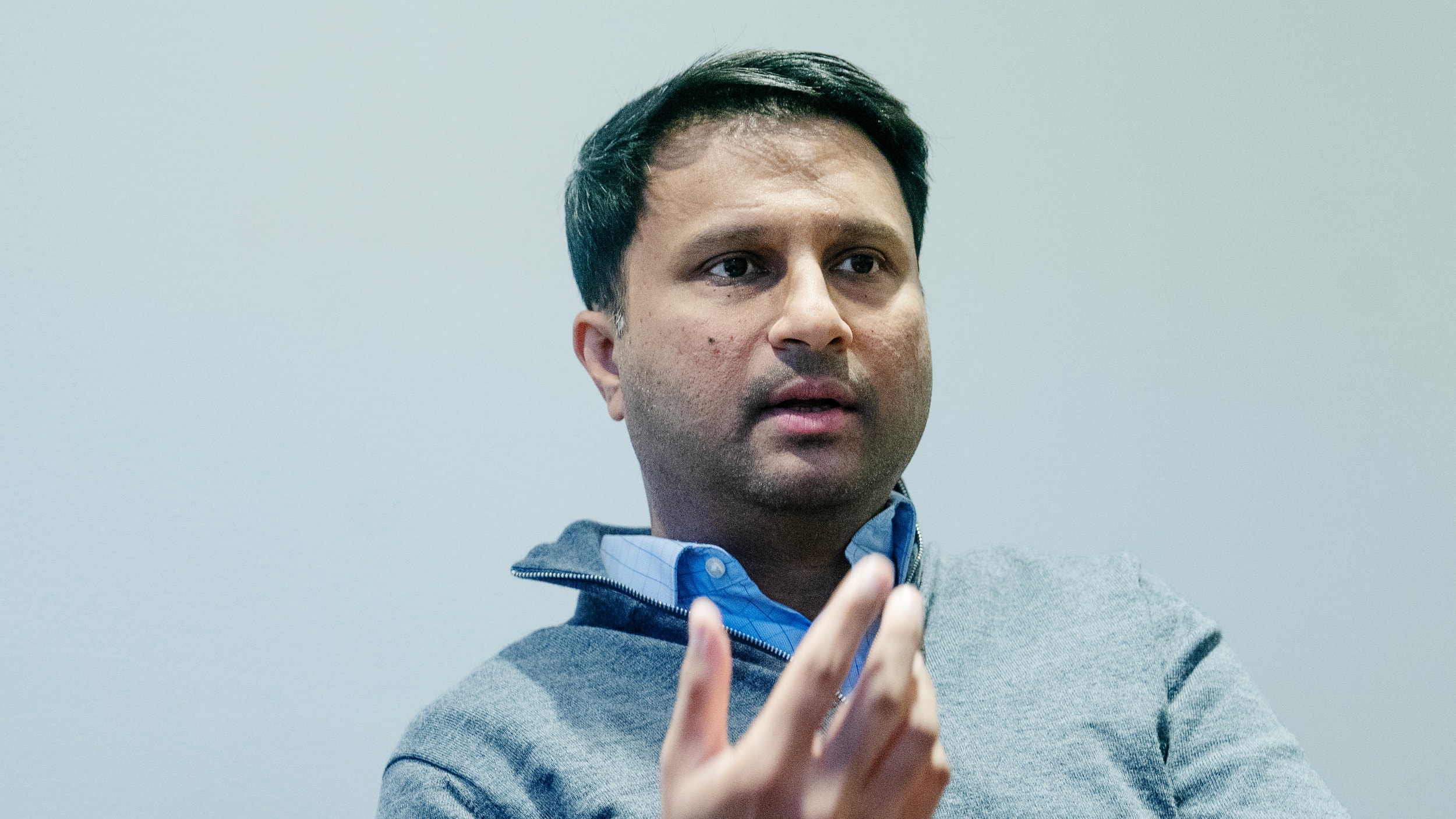 Porträtt av Rishit Jhunjhunwala, en man i grå tröja med blå halsduk, som gestikulerar medan han talar mot en ljus bakgrund.