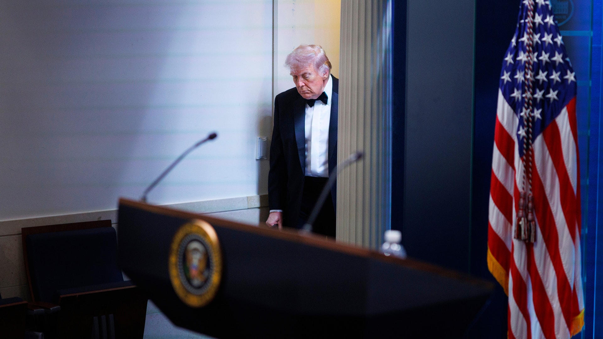En äldre man i smoking står vid ett podium med presidentens sigill. En amerikansk flagga syns i bakgrunden.