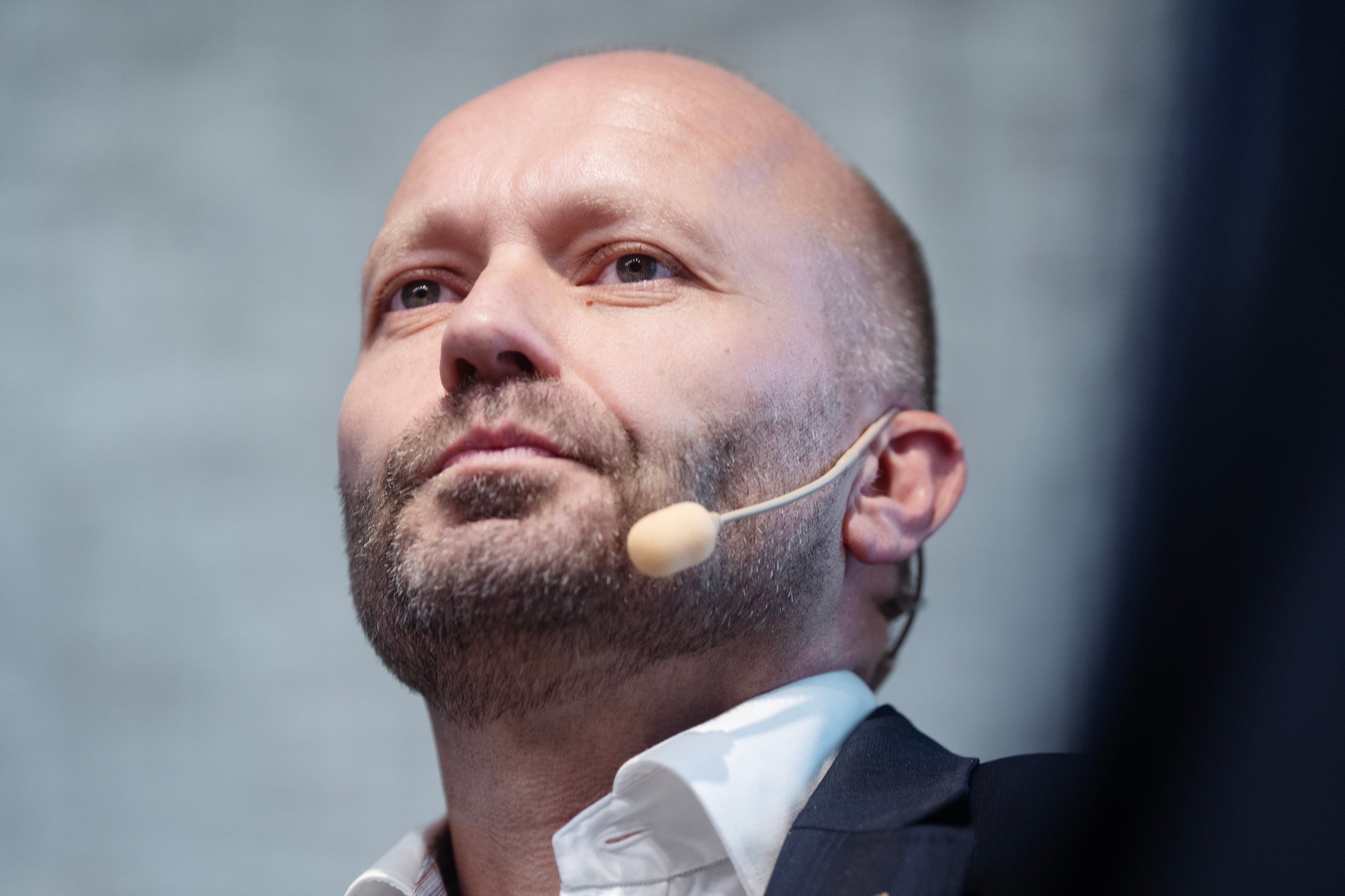 Närbild på Ivar Vatne, en skallig man med skäggstubb och headset, som tittar uppåt under ett seminarium.