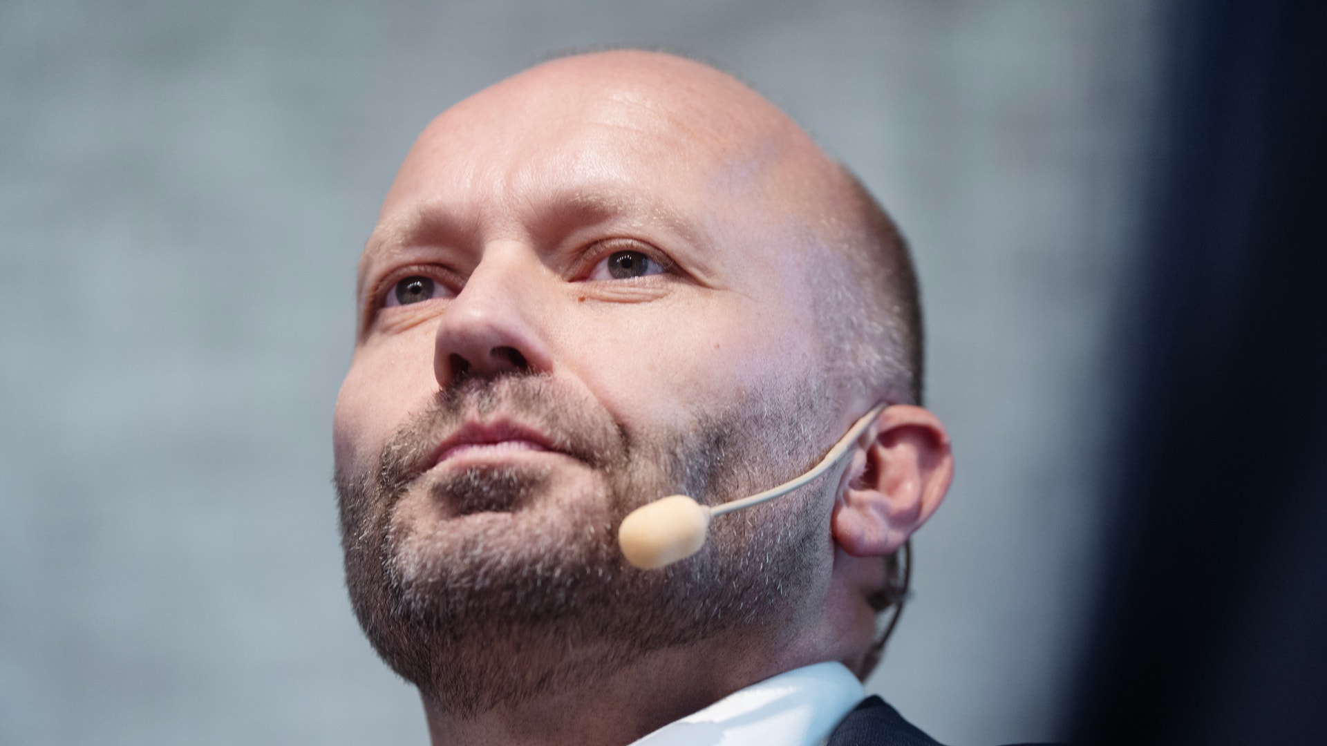 Närbild på Ivar Vatne, en skallig man med skäggstubb och headset, som tittar uppåt under ett seminarium.