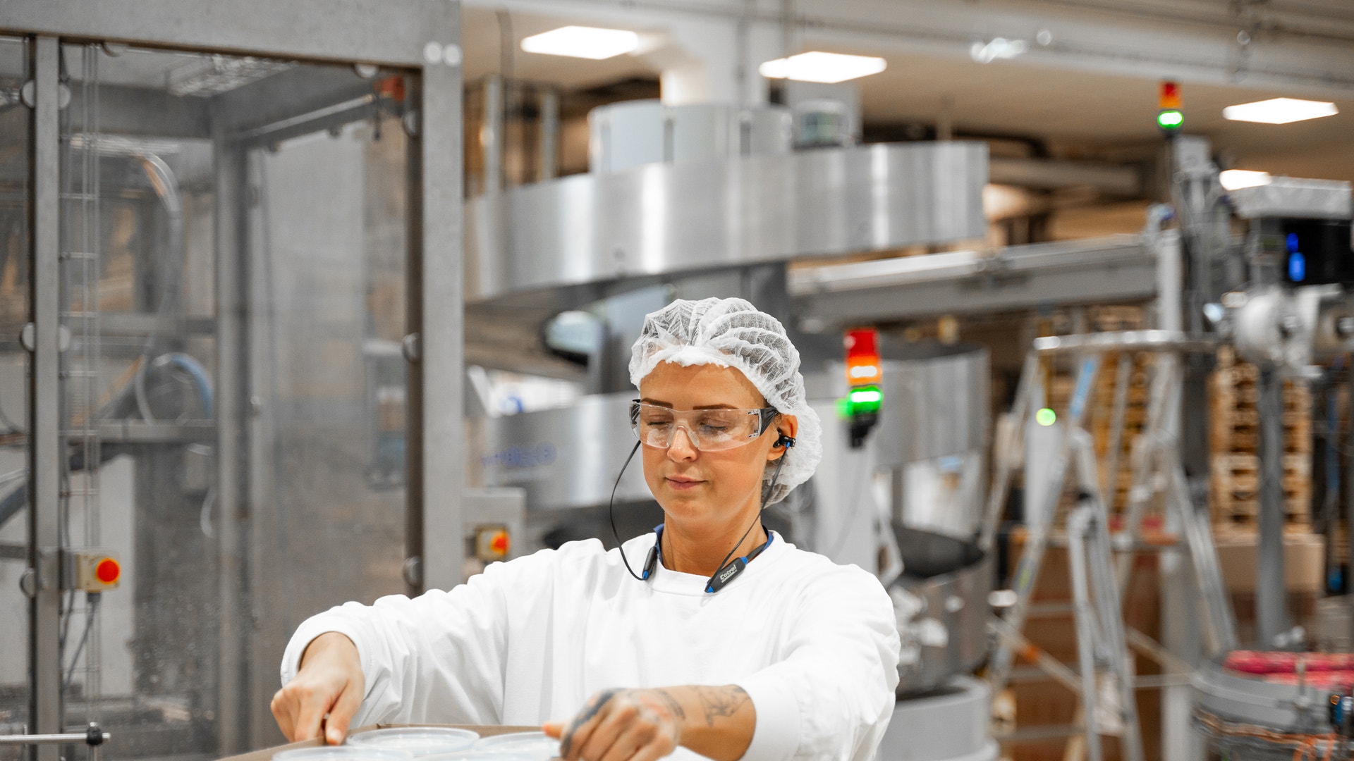 Medarbetare i vita arbetskläder och hårnät arbetar vid en maskin i en mejeriproduktion.