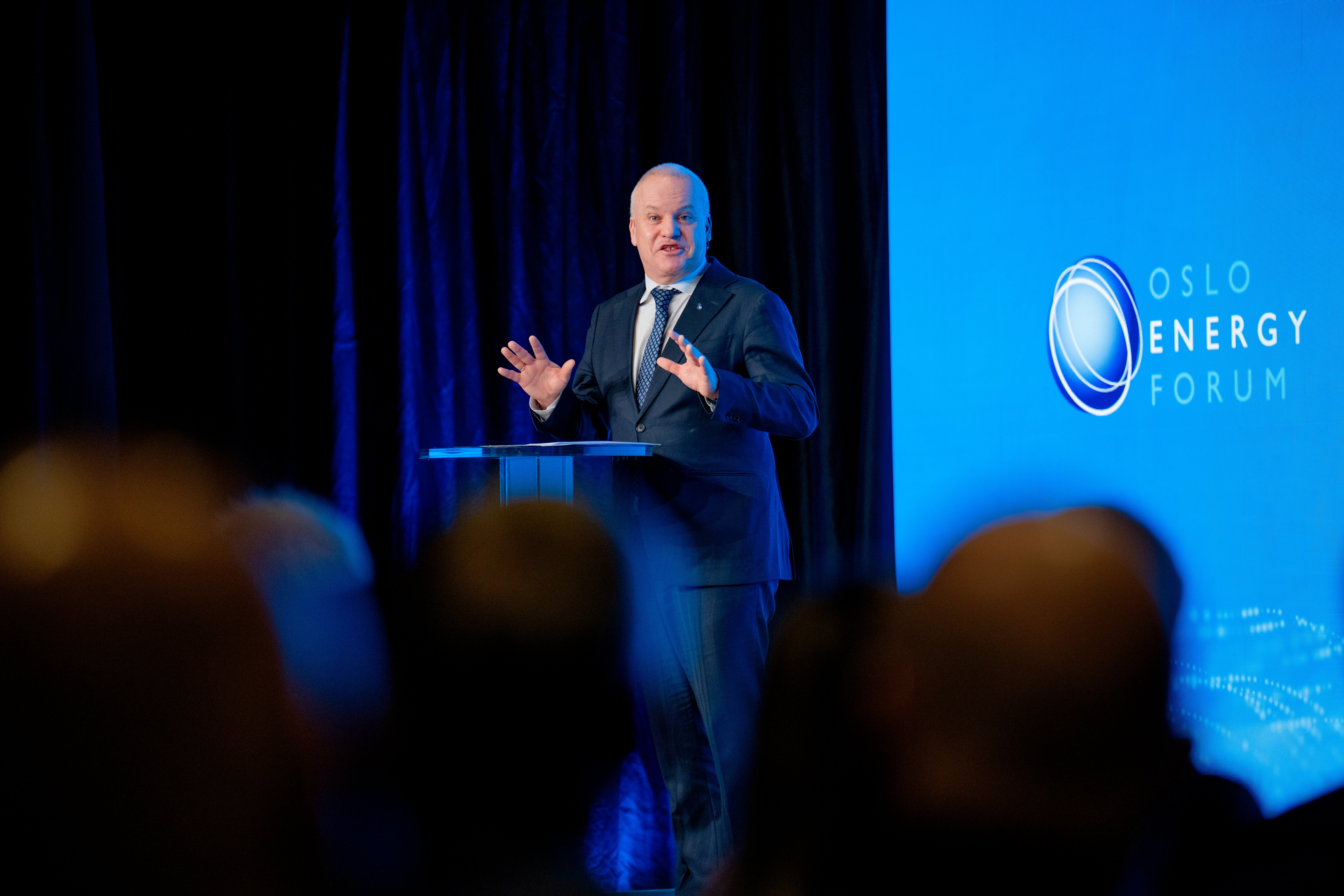 Man i mörk kostym talar vid ett podium på Oslo Energy Forum framför publik.
