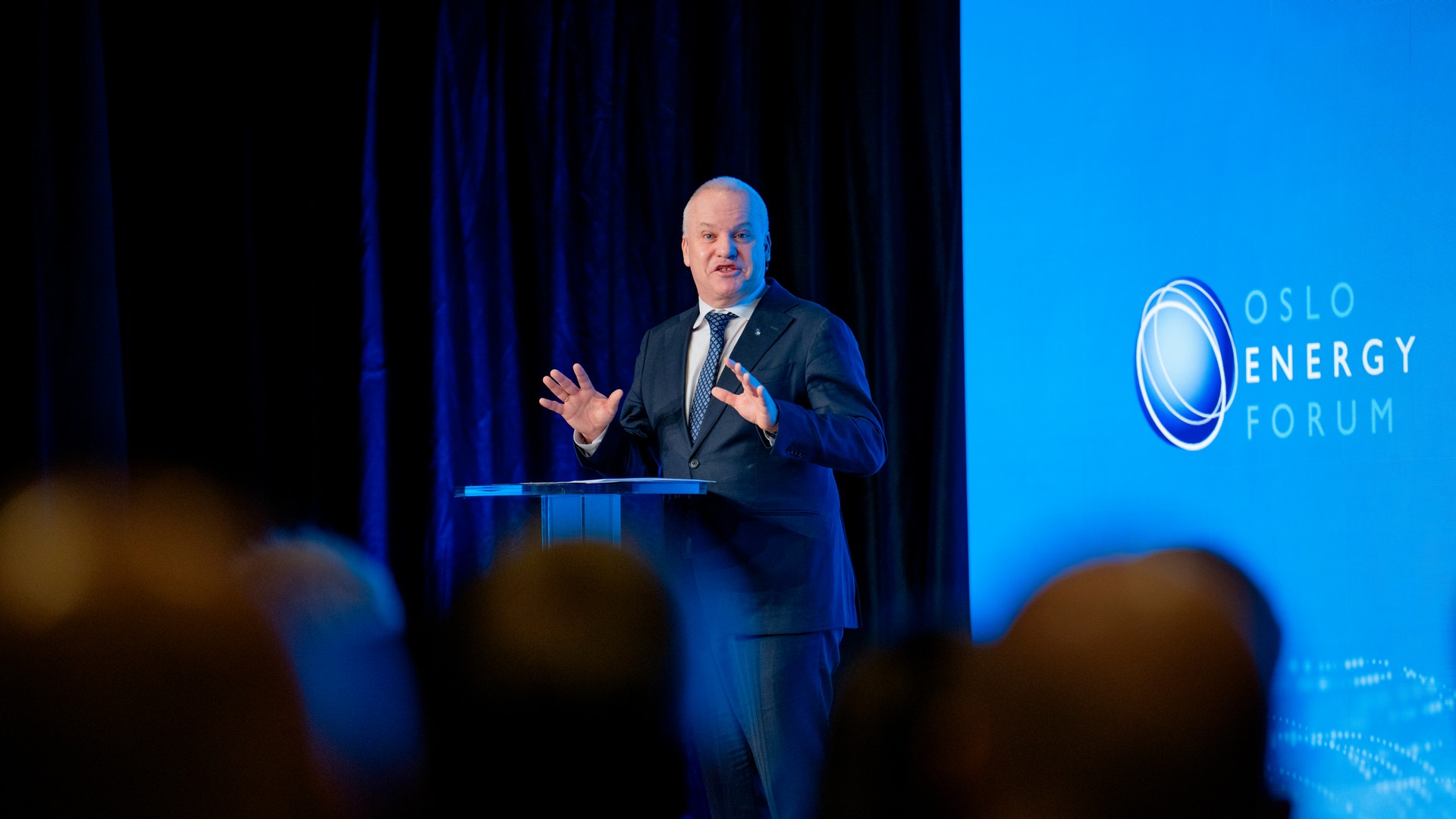 Man i mörk kostym talar vid ett podium på Oslo Energy Forum framför publik.