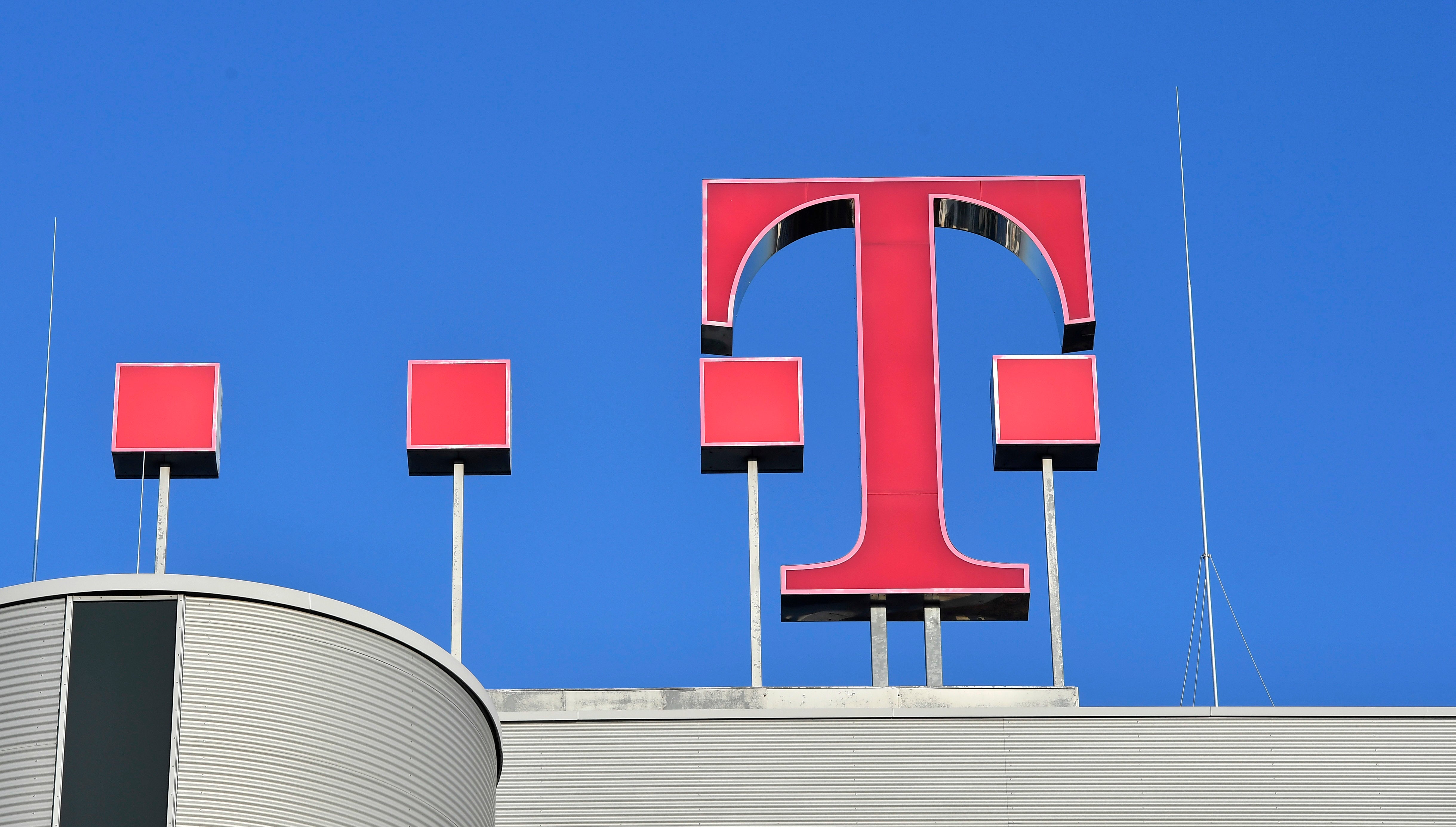 Bilden visar en stor röd T-logotyp på en byggnad mot blå himmel.