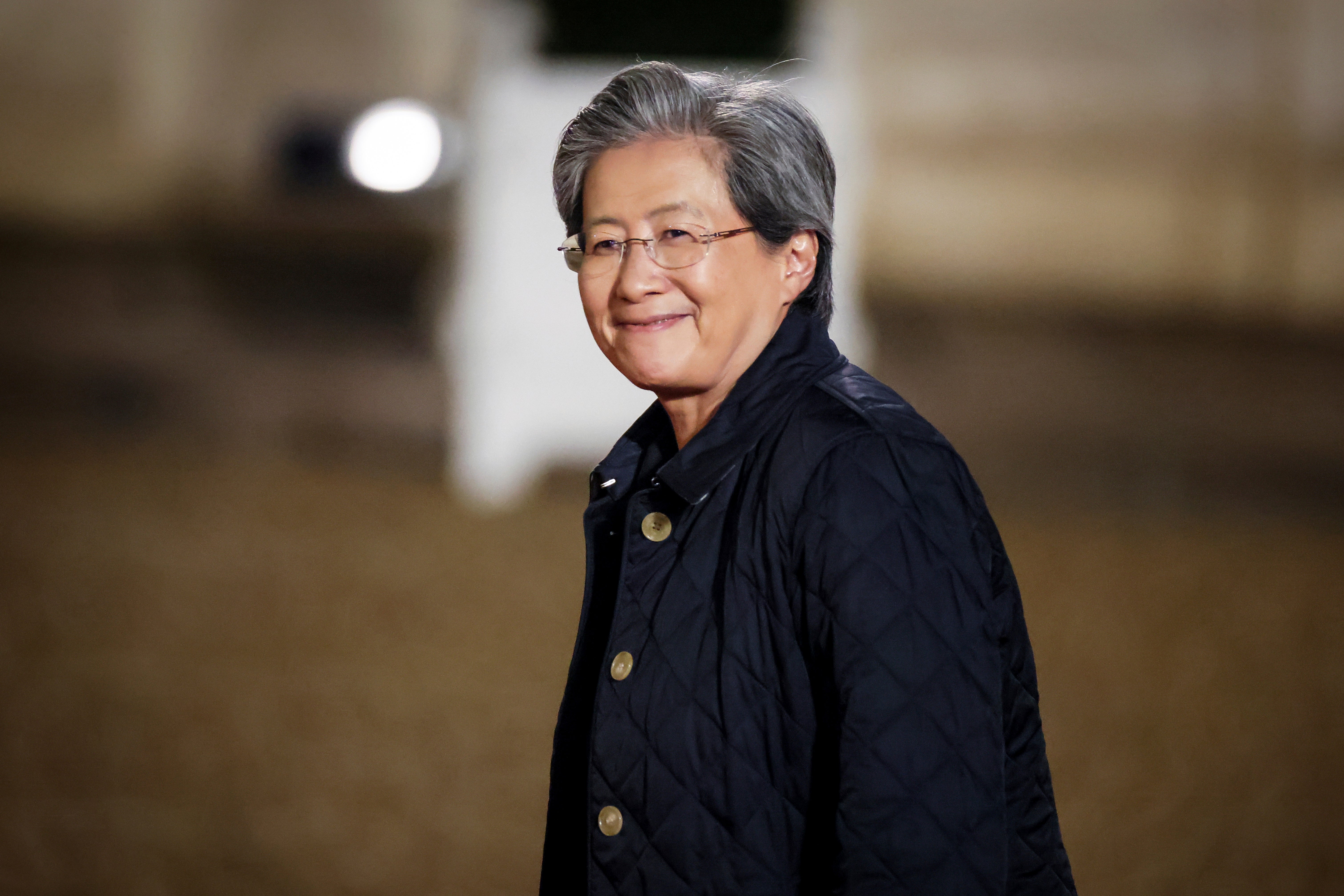 Porträtt av en person med glasögon och mörkblå jacka mot en suddig bakgrund inomhus.