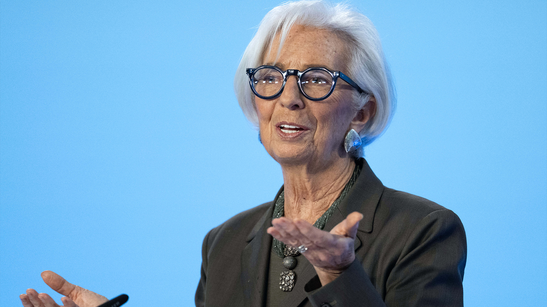 Porträttfoto av Christine Lagarde, en äldre kvinna med vitt hår och glasögon, klädd i mörk kostym mot blå bakgrund.