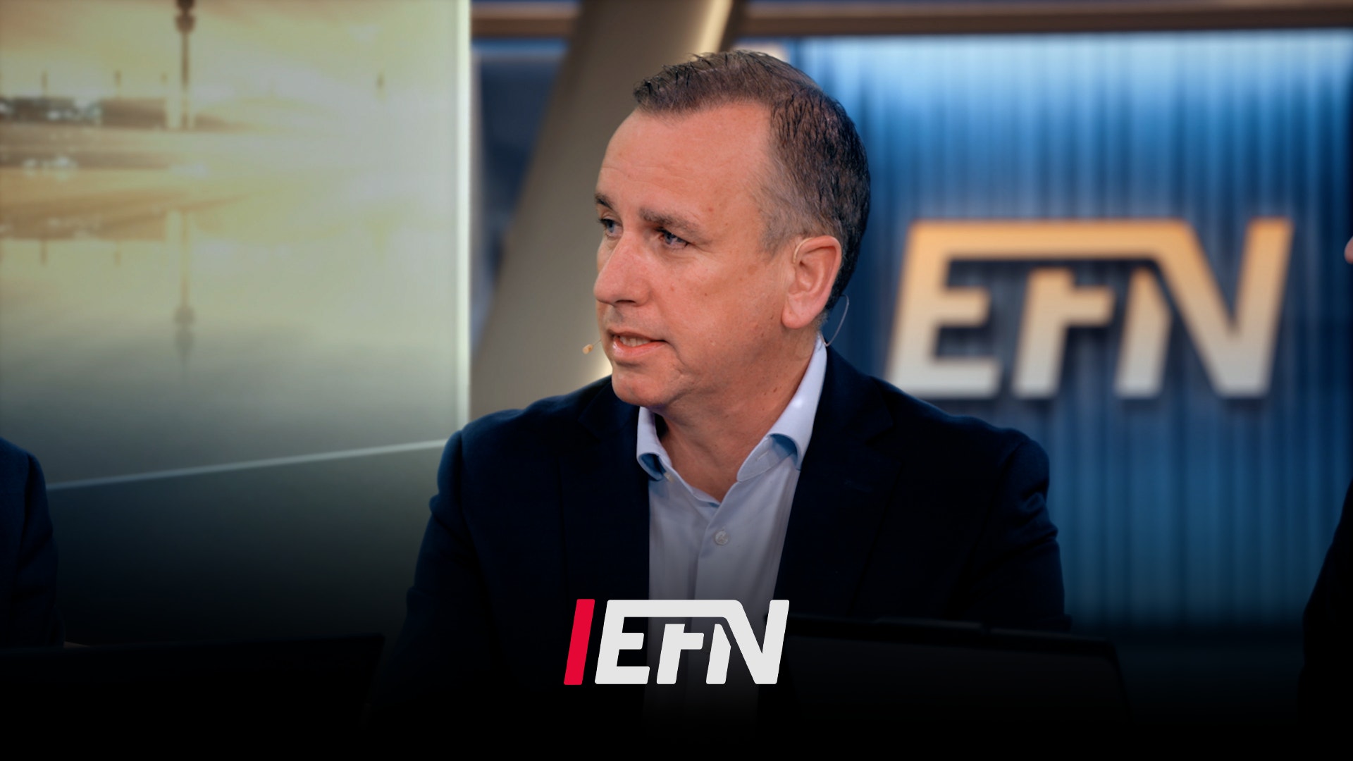 Man i mörkblå blazer sitter i TV-studio under en intervju. EFN-logon syns i bakgrunden.