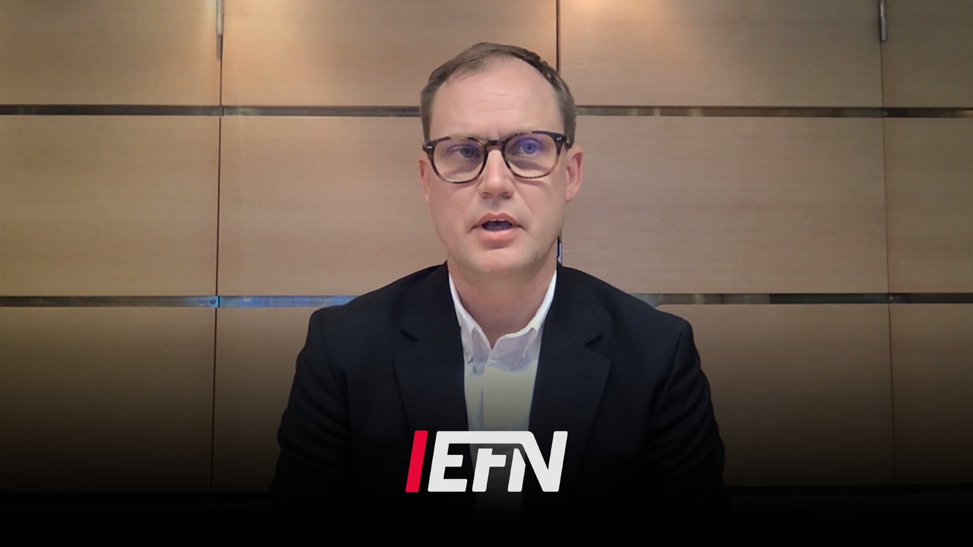 Man i glasögon och mörk blazer talar framför en vägg med EFN-logotyp i en studiomiljö.