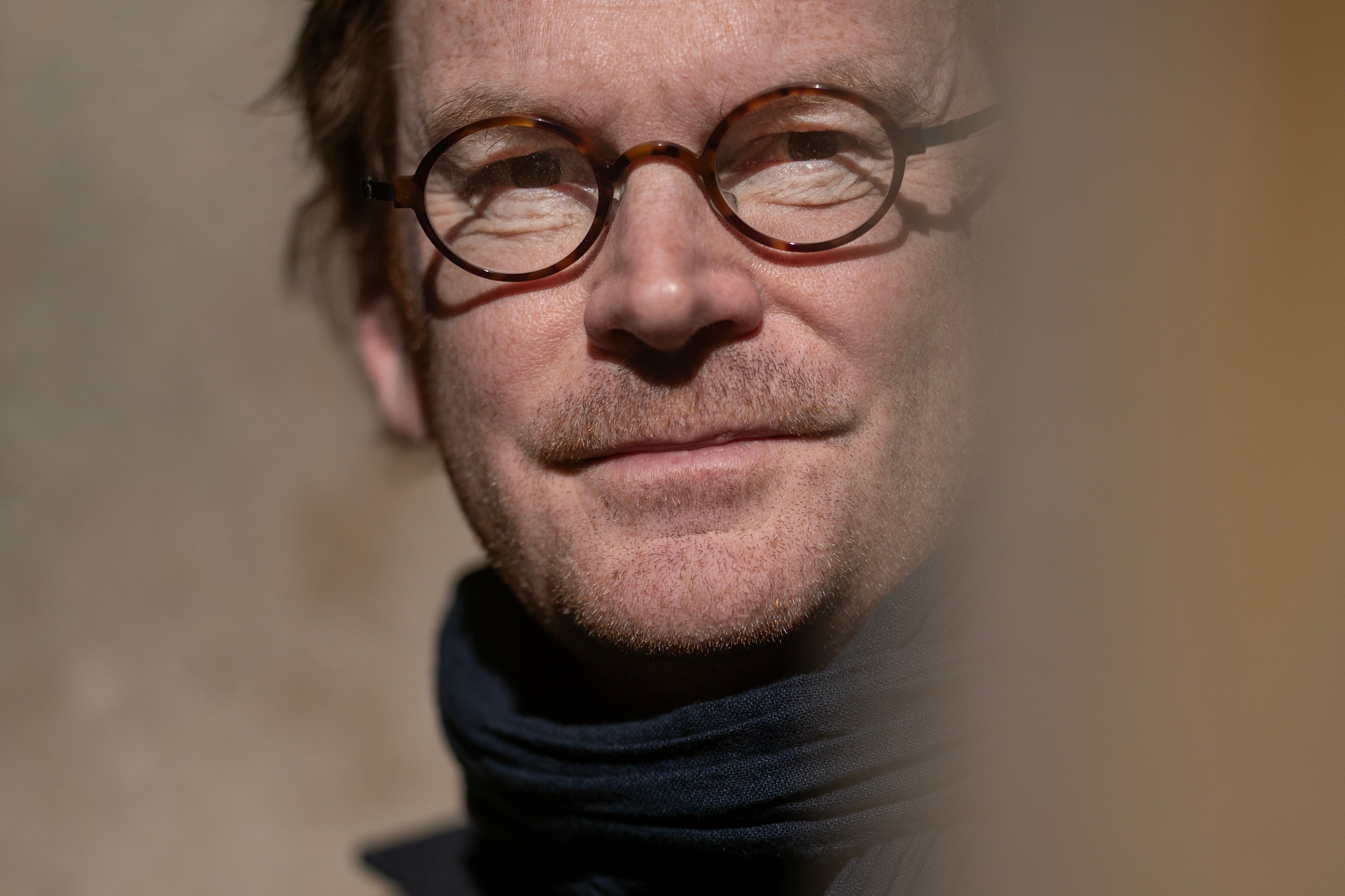 Porträtt av en man med glasögon och svart polotröja mot en neutral bakgrund.