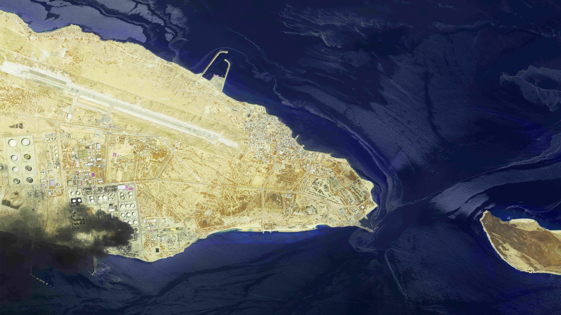 Satellitbild av en gul-beige ö omgiven av djupblått vatten. Ön har vägar och strukturer synliga från ovan.