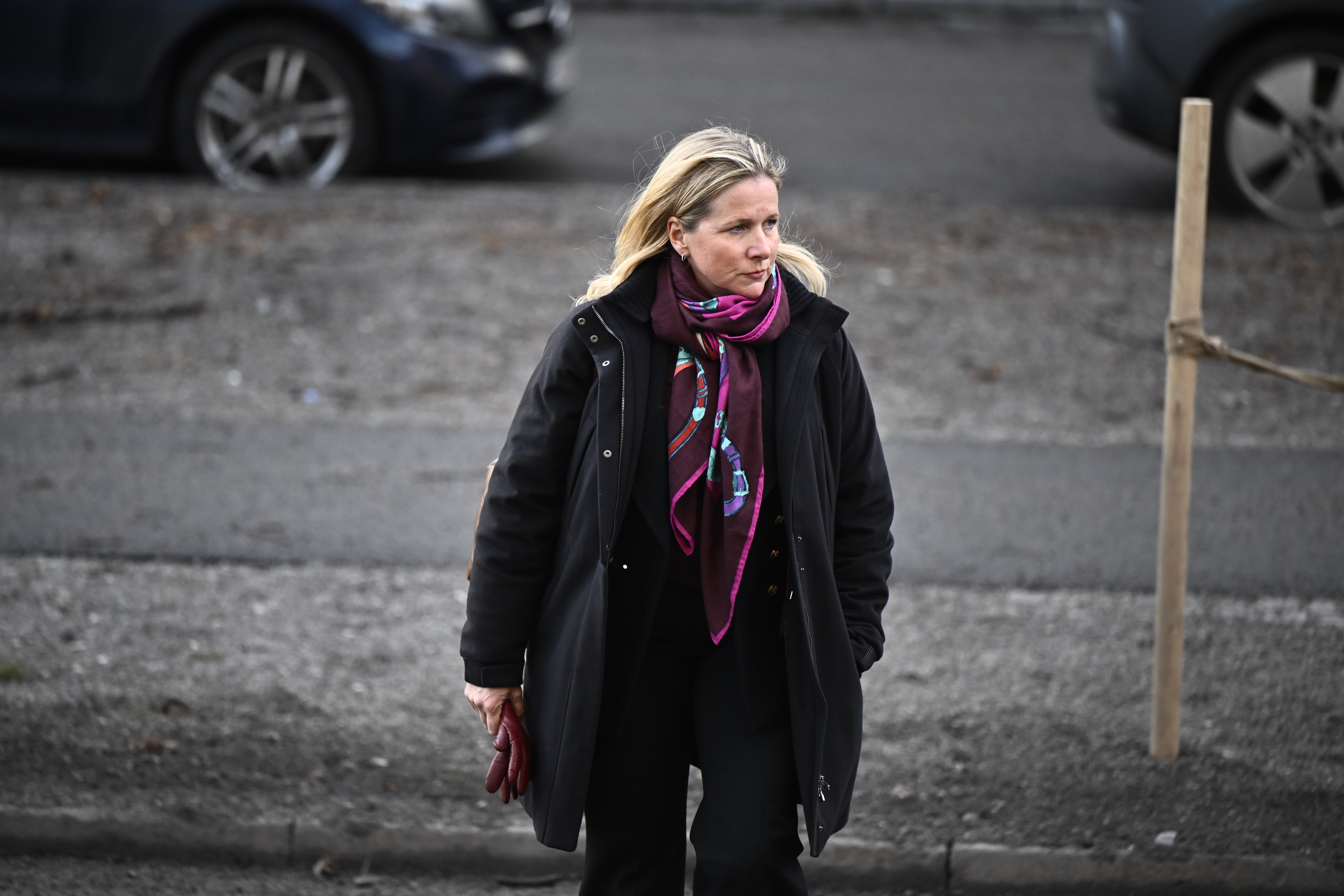 En kvinna i svart kappa och lila halsduk går på en parkeringsplats.