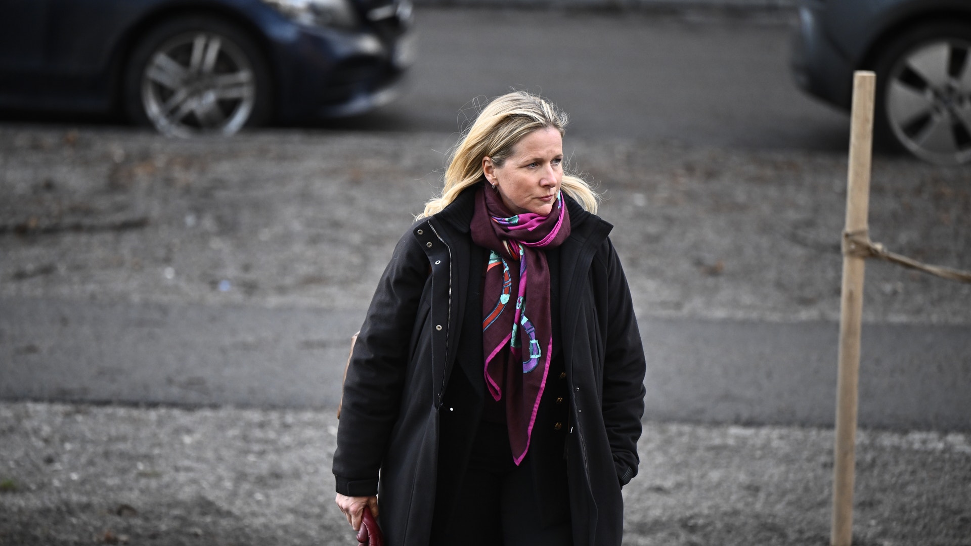 En kvinna i svart kappa och lila halsduk går på en parkeringsplats.