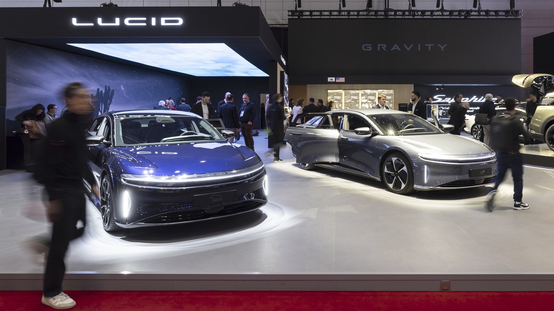 Två elbilar på en bilutställning med besökare som tittar på fordonen.