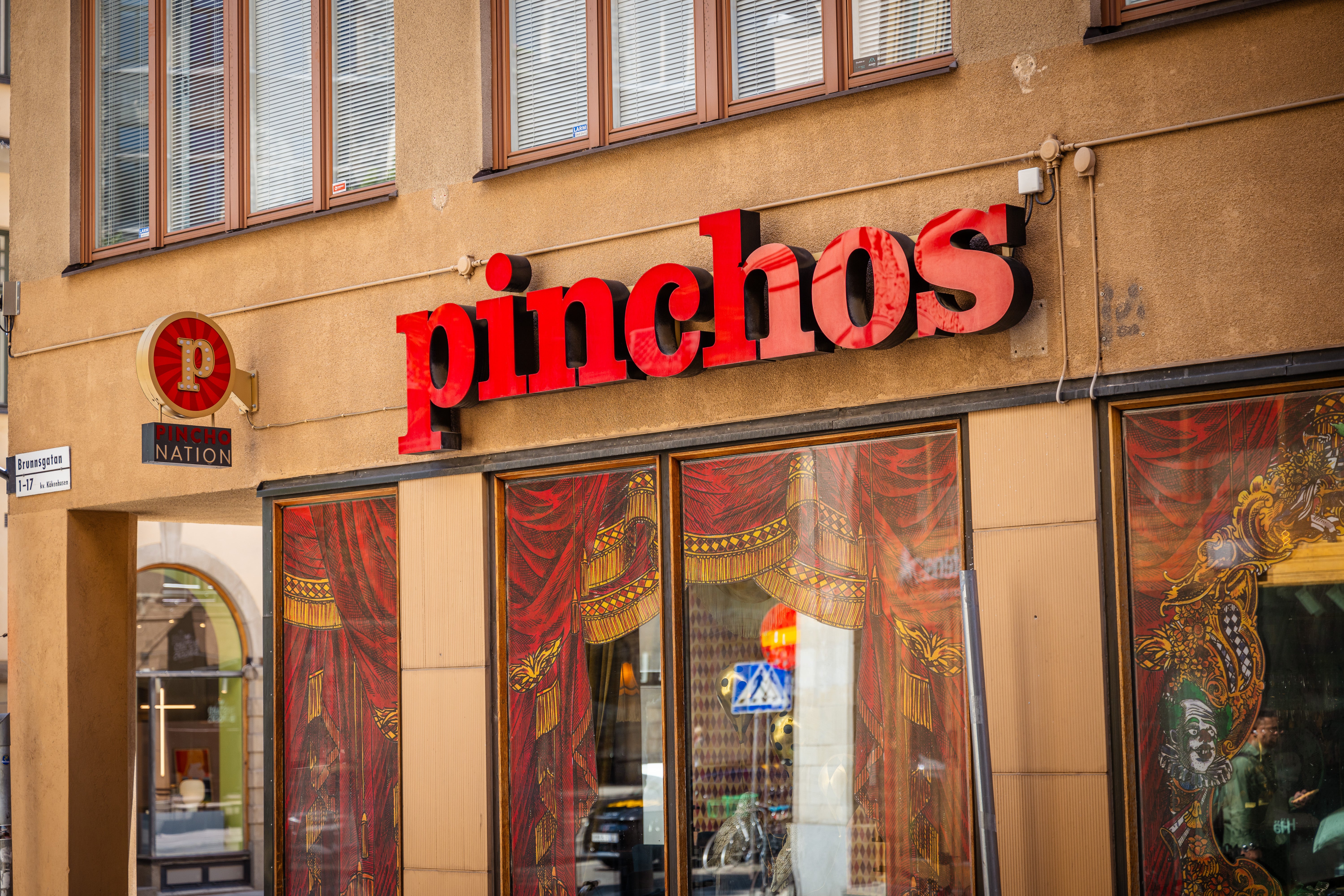 Fasaden på restaurangen Pinchos med rött skylttext på beige vägg och dekorerade röda dörrar.