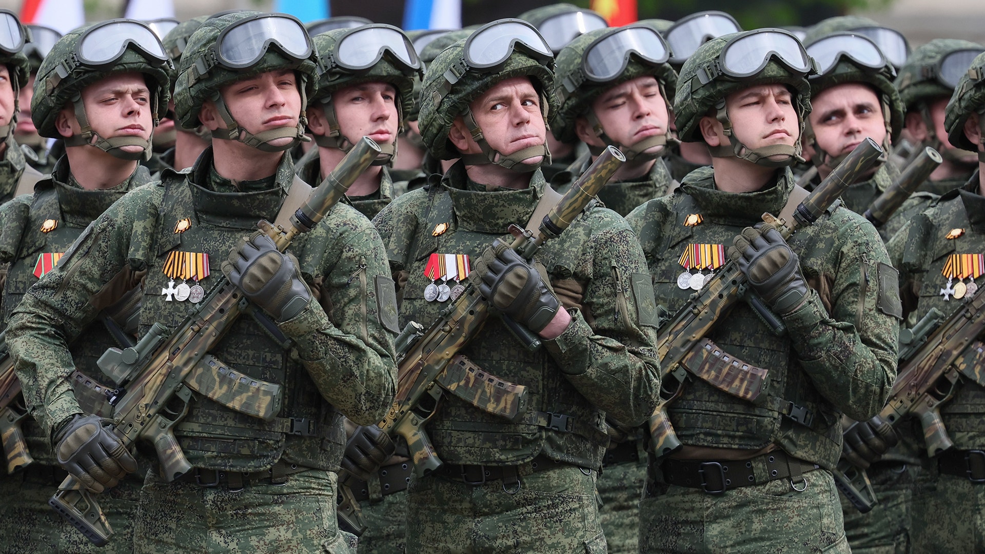 En grupp ryska soldater i grön kamouflageuniform står tätt tillsammans i formation. De bär hjälmar, automatvapen och militärmedaljer på bröstet.