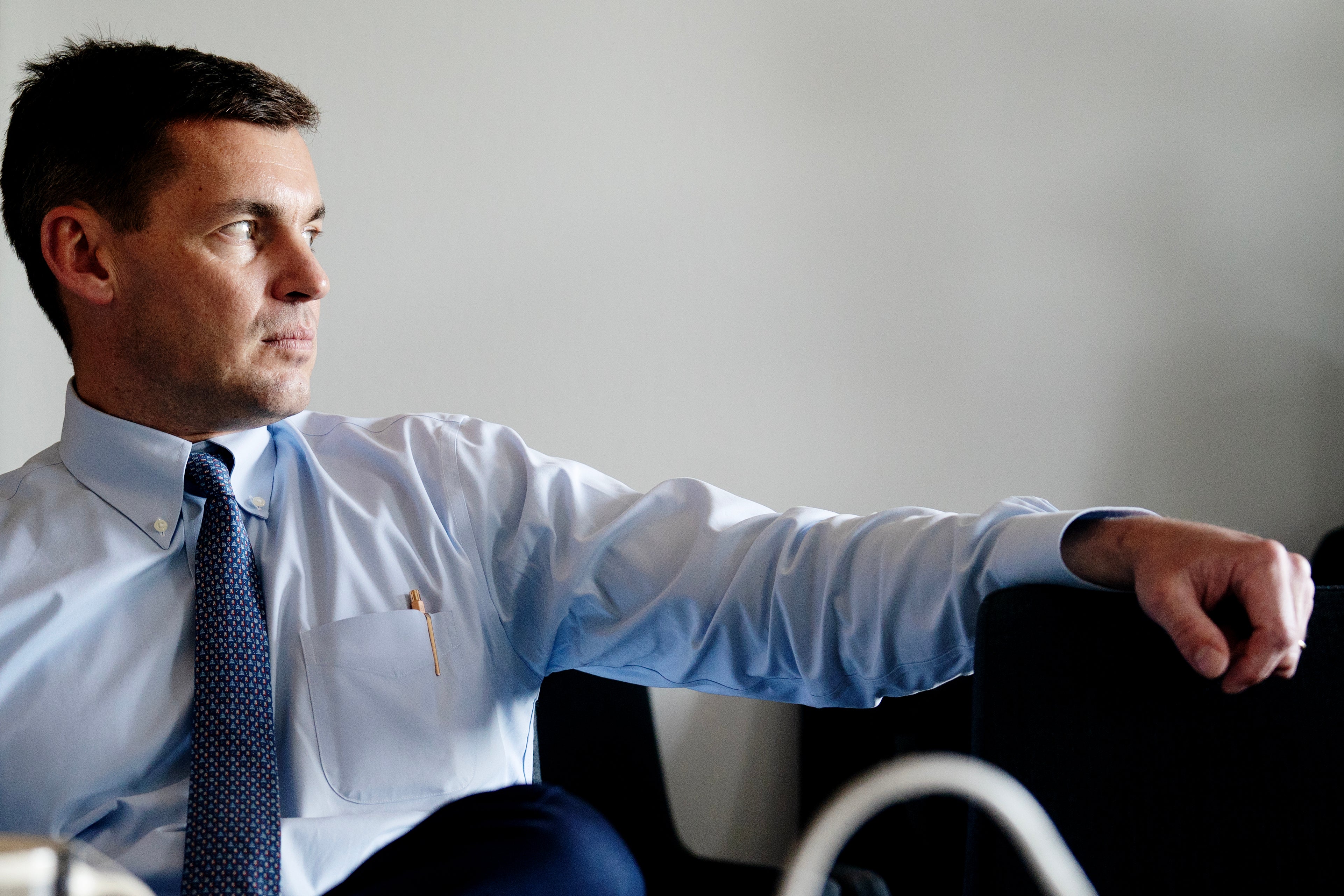 Man i ljusblå skjorta och slips sitter och sträcker ut armen framför sig