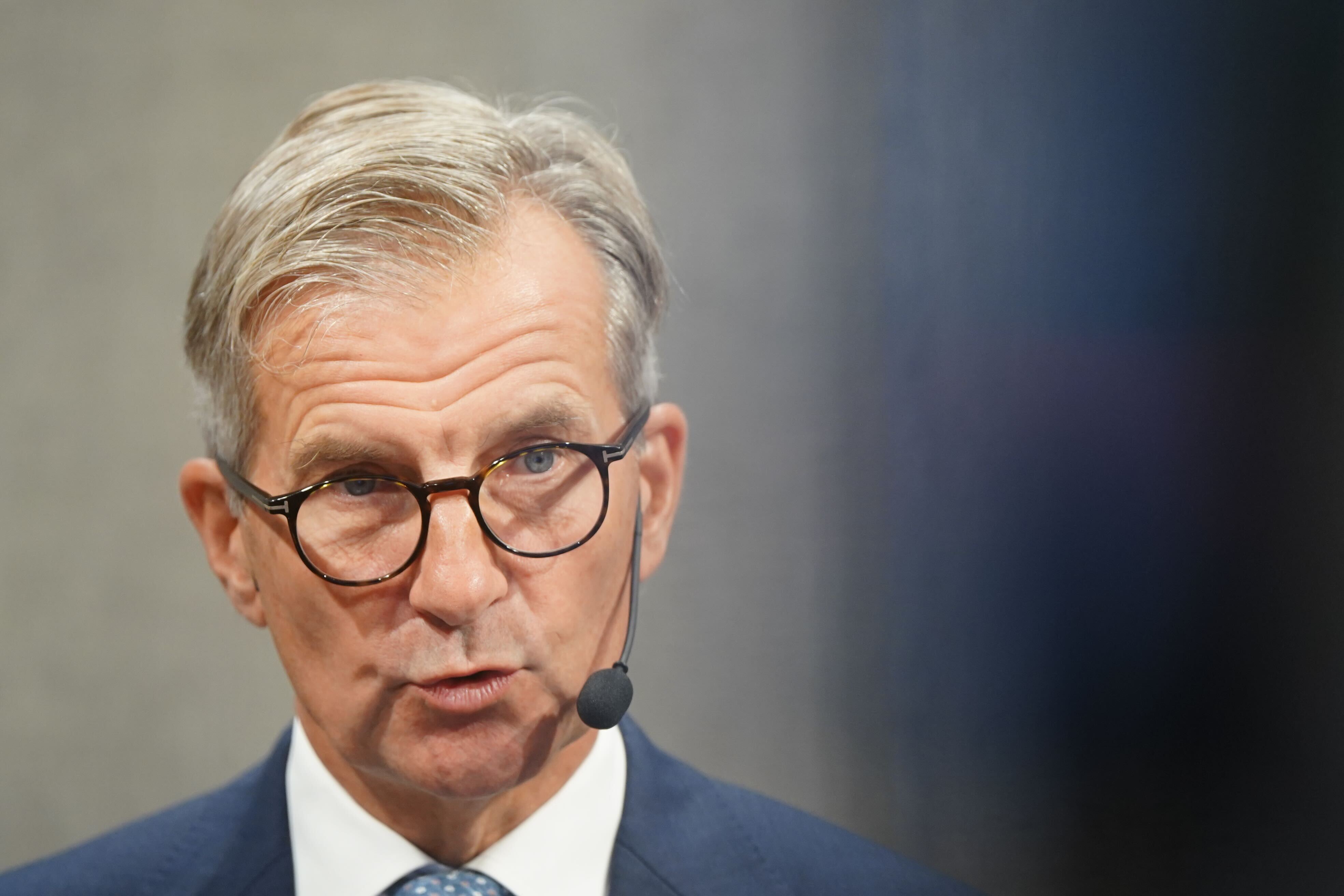 En man i glasögon och mörkblå kostym talar vid en mikrofon