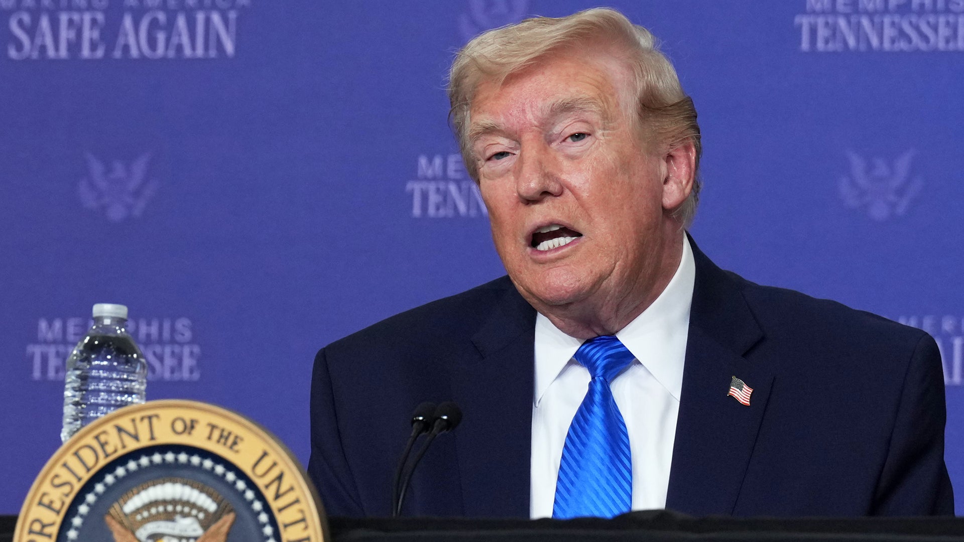 En man i mörk kostym och blå slips talar vid ett podium med presidentens sigill framför en blå bakgrund.