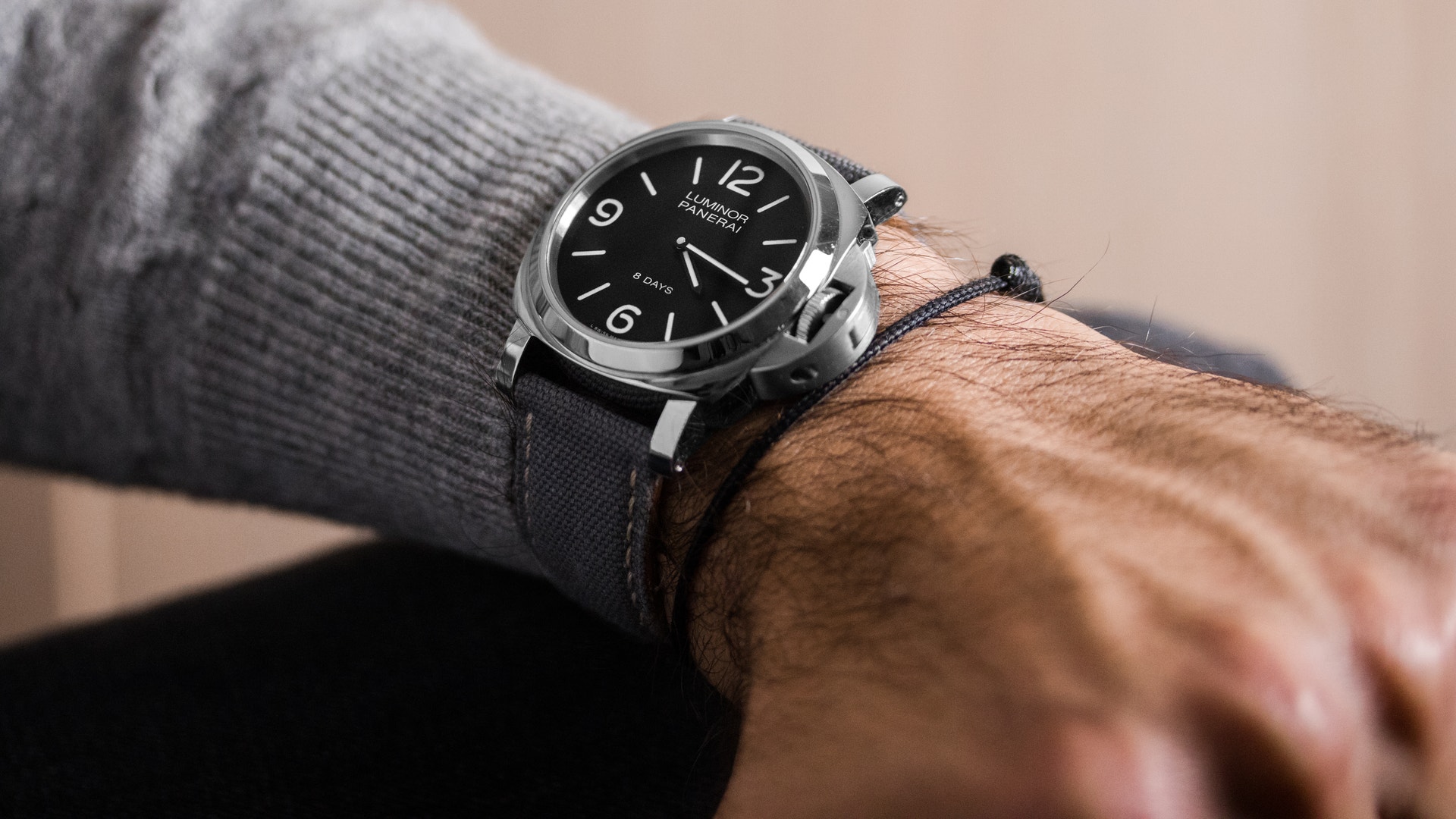Armbandsur med svart urtavla och läderrem på en persons handled. Personen bär en grå stickad tröja.