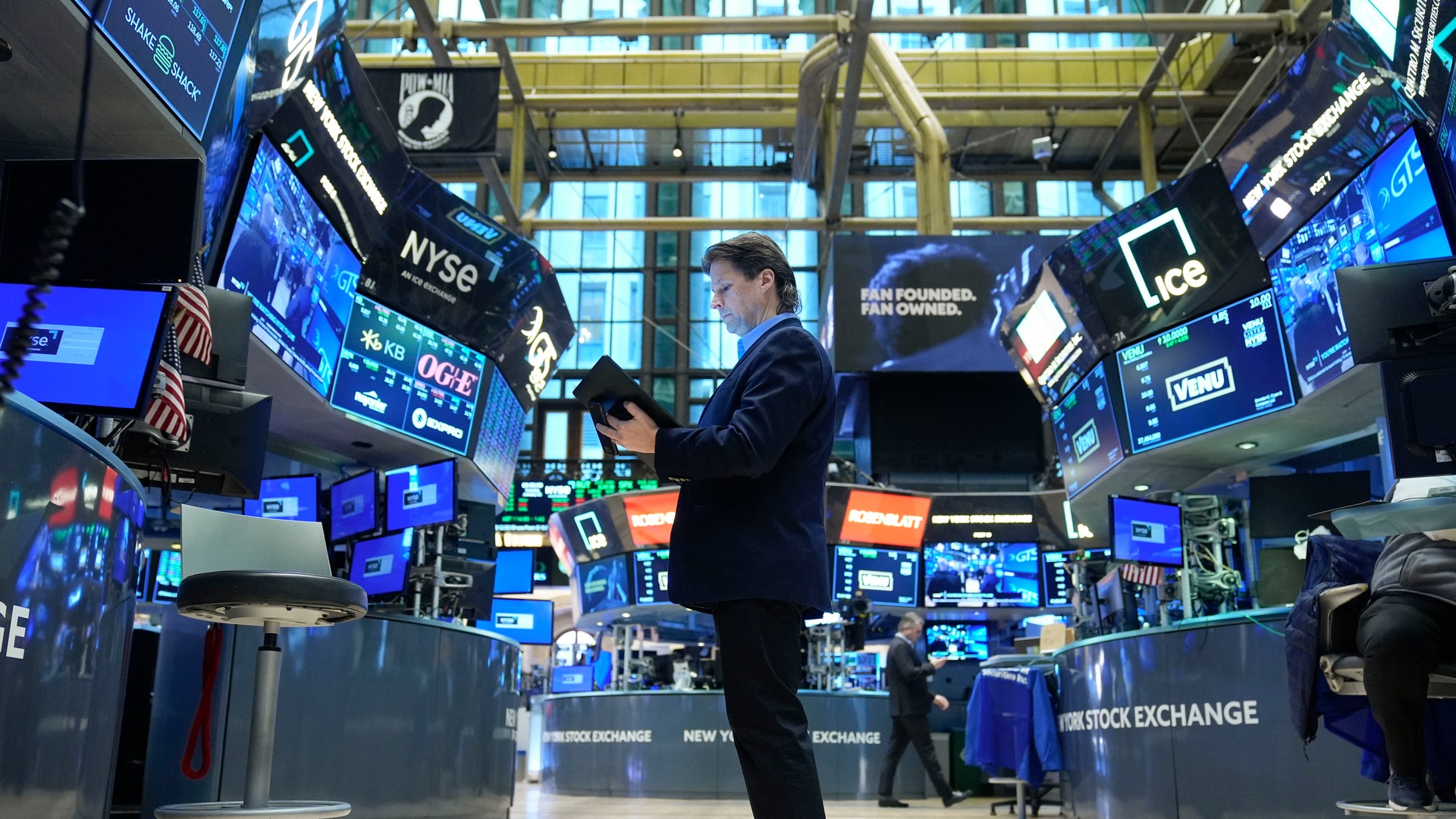 Handlare på en börshandelsplats omgiven av digitala skärmar och handelsstationer.