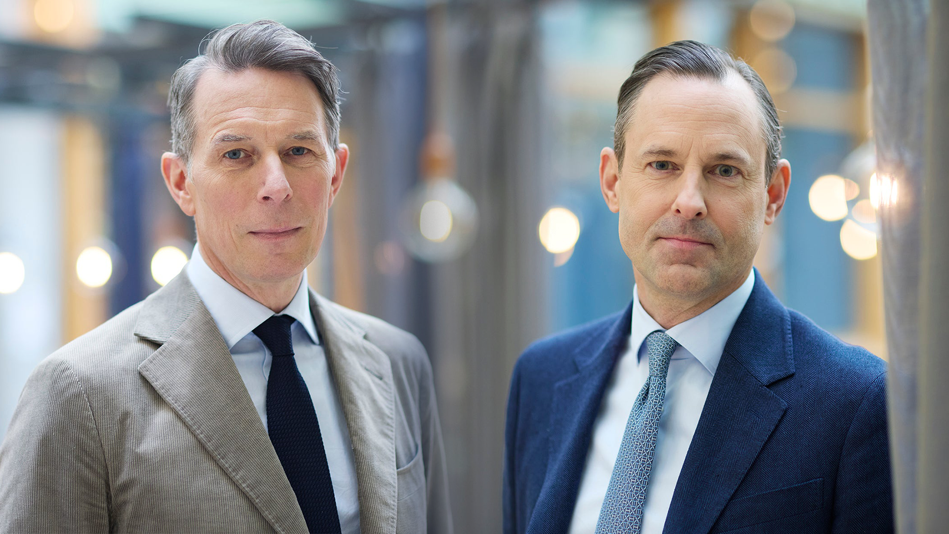 Två män i affärskläder står sida vid sida i en modern kontorsmiljö.