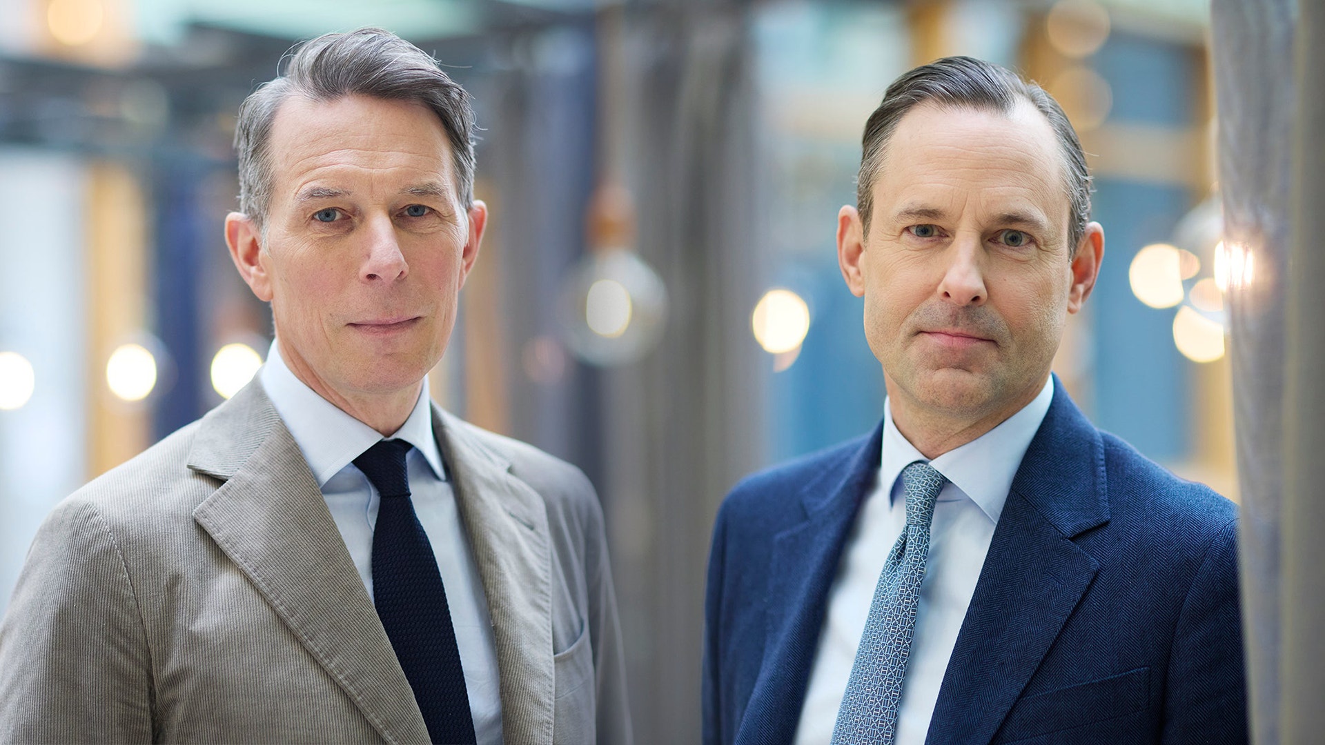 Två män i affärskläder står sida vid sida i en modern kontorsmiljö.
