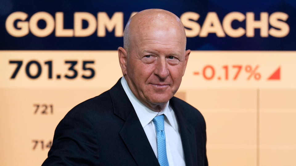 Porträttfoto av David Solomon, VD för Goldman Sachs, i mörkblå kostym och ljusblå slips framför Goldman Sachs-logotyp och aktiekurser som visar 701.35 och -0.17% förändring.