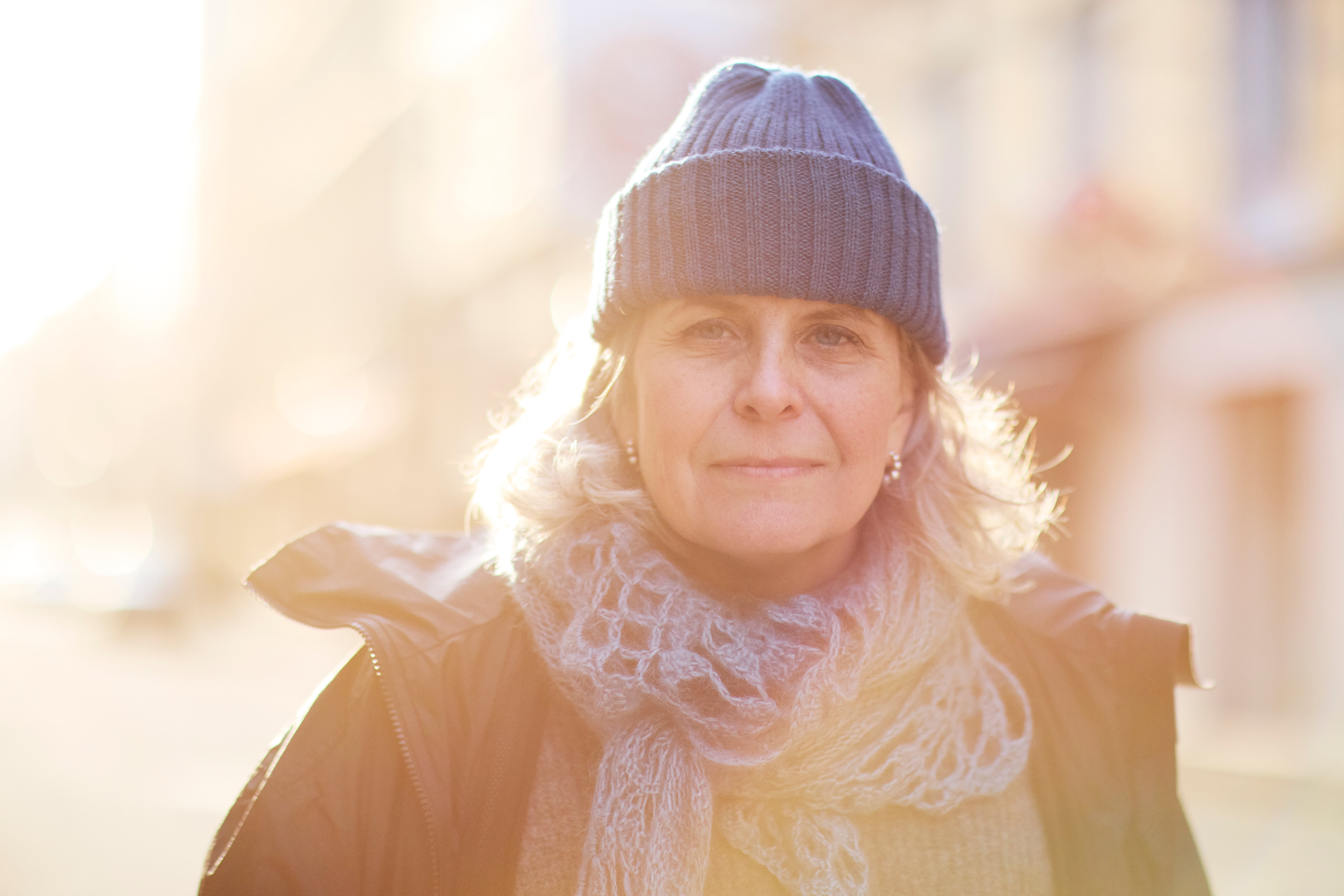 Porträtt av en kvinna med mössa och halsduk i soligt väder utomhus.