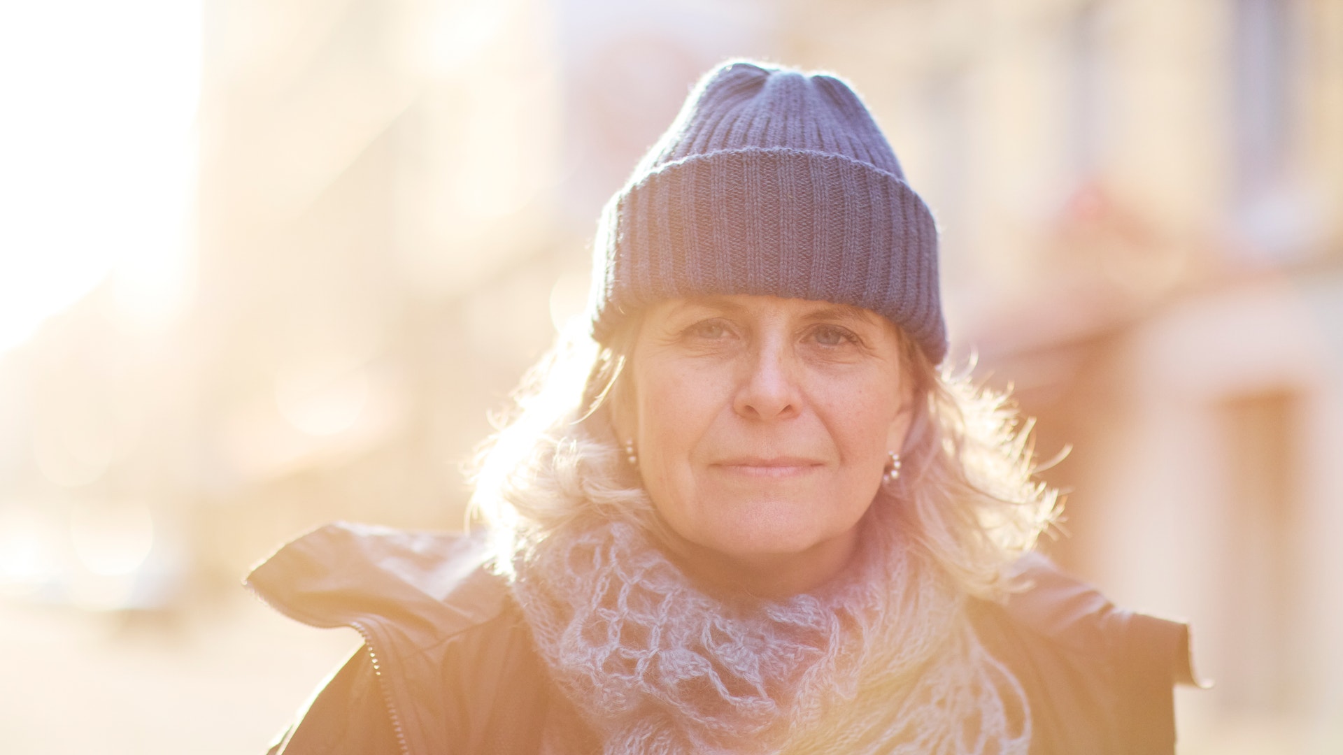 Porträtt av en kvinna med mössa och halsduk i soligt väder utomhus.