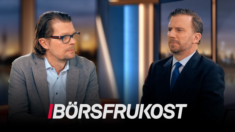 Två män i affärskläder diskuterar vid ett bord i en studiomiljö. Mannen till vänster bär glasögon och grå kavaj över ljusblå skjorta. Mannen till höger bär mörkblå kostym och blå slips. I bakgrunden syns en stadshorisont och blå belysning. Texten "BÖRSFRUKOST" visas längst ned i bild.