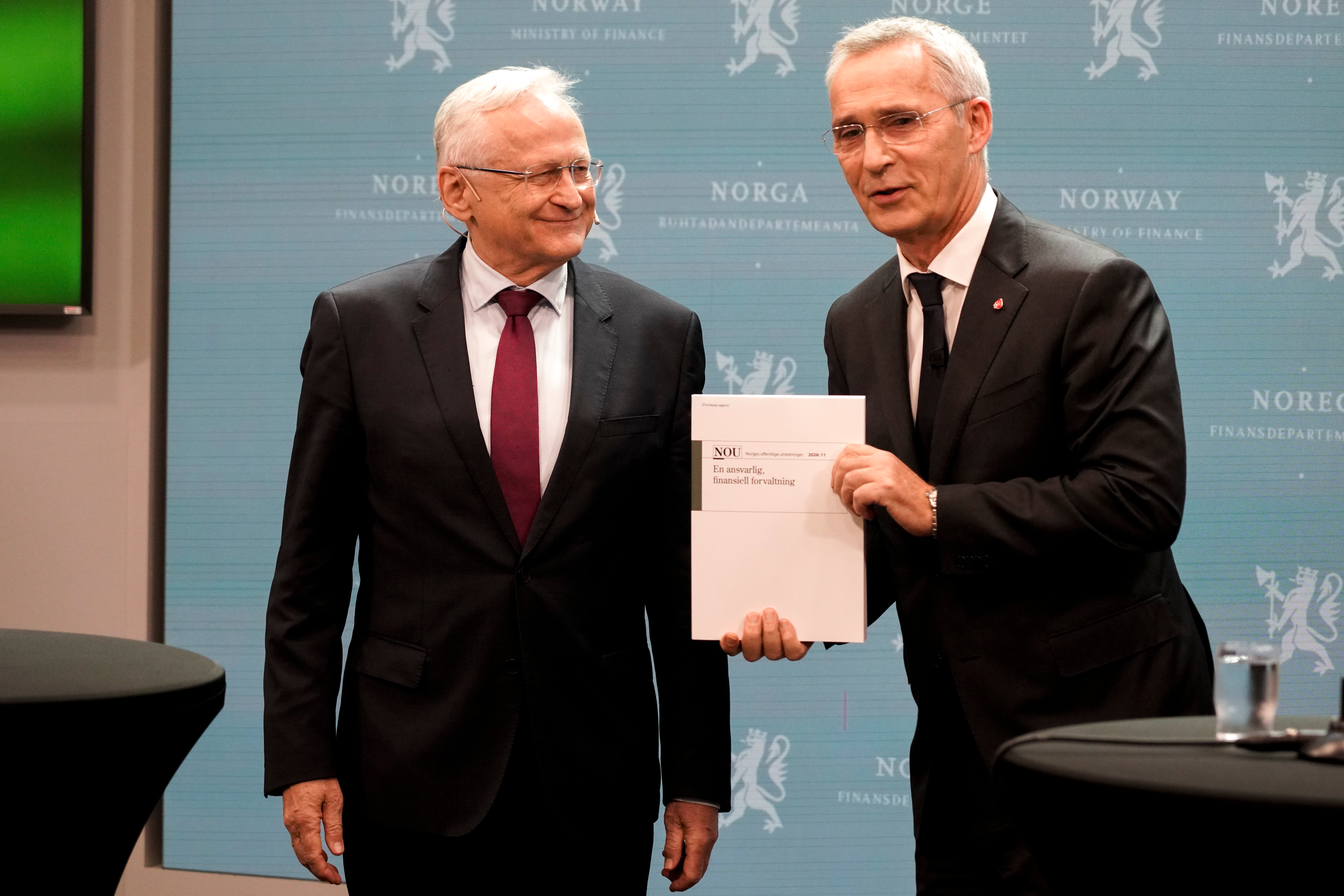 Två män i mörka kostymer står bredvid varandra framför en blå vägg med texten Norge och Finansdepartementet. Mannen till höger håller upp en rapport.