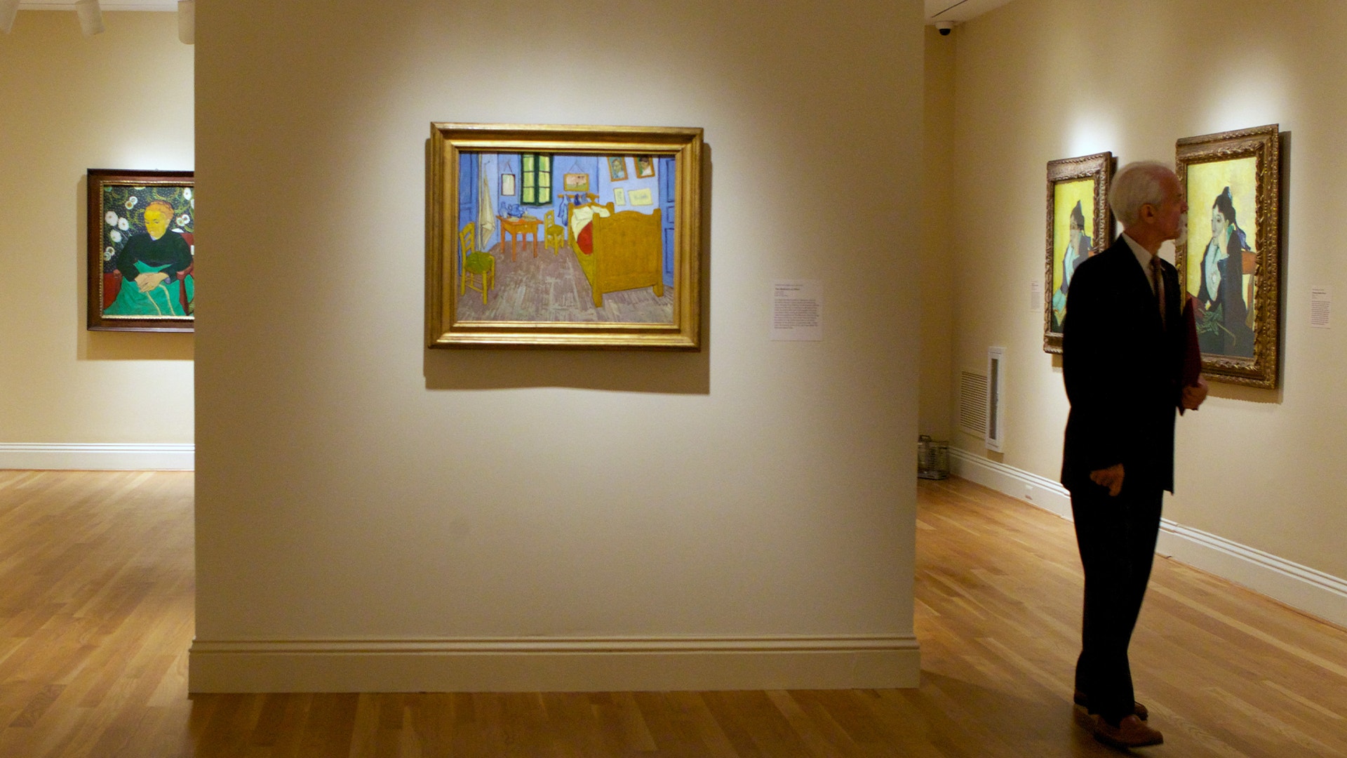 En person betraktar tavlor i ett konstgalleri, bland annat en målning som liknar van Goghs sovrum.
