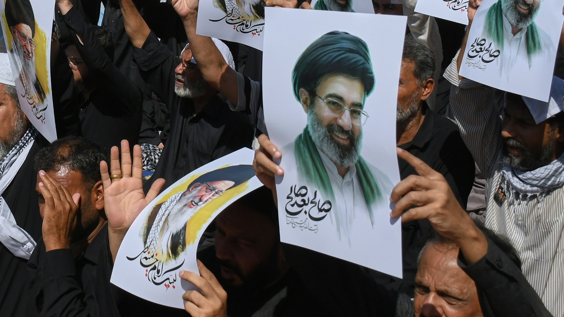 Folkmassa som håller porträtt och banderoller vid en samling eller demonstration.