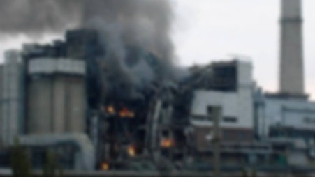 Industrianläggning i brand med flammor och rök som stiger upp från byggnaden.