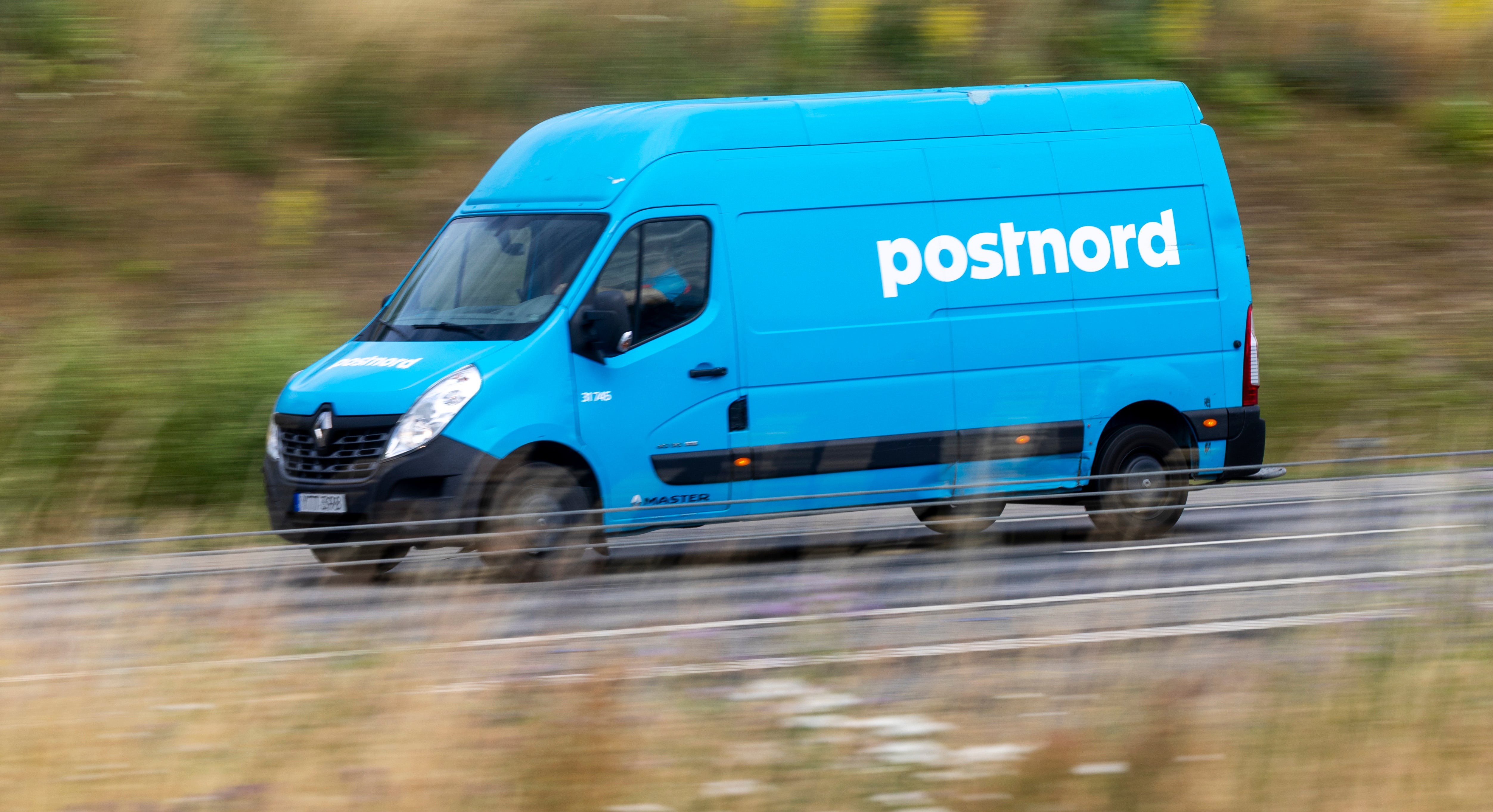 En blå Postnord-skåpbil kör på en väg.