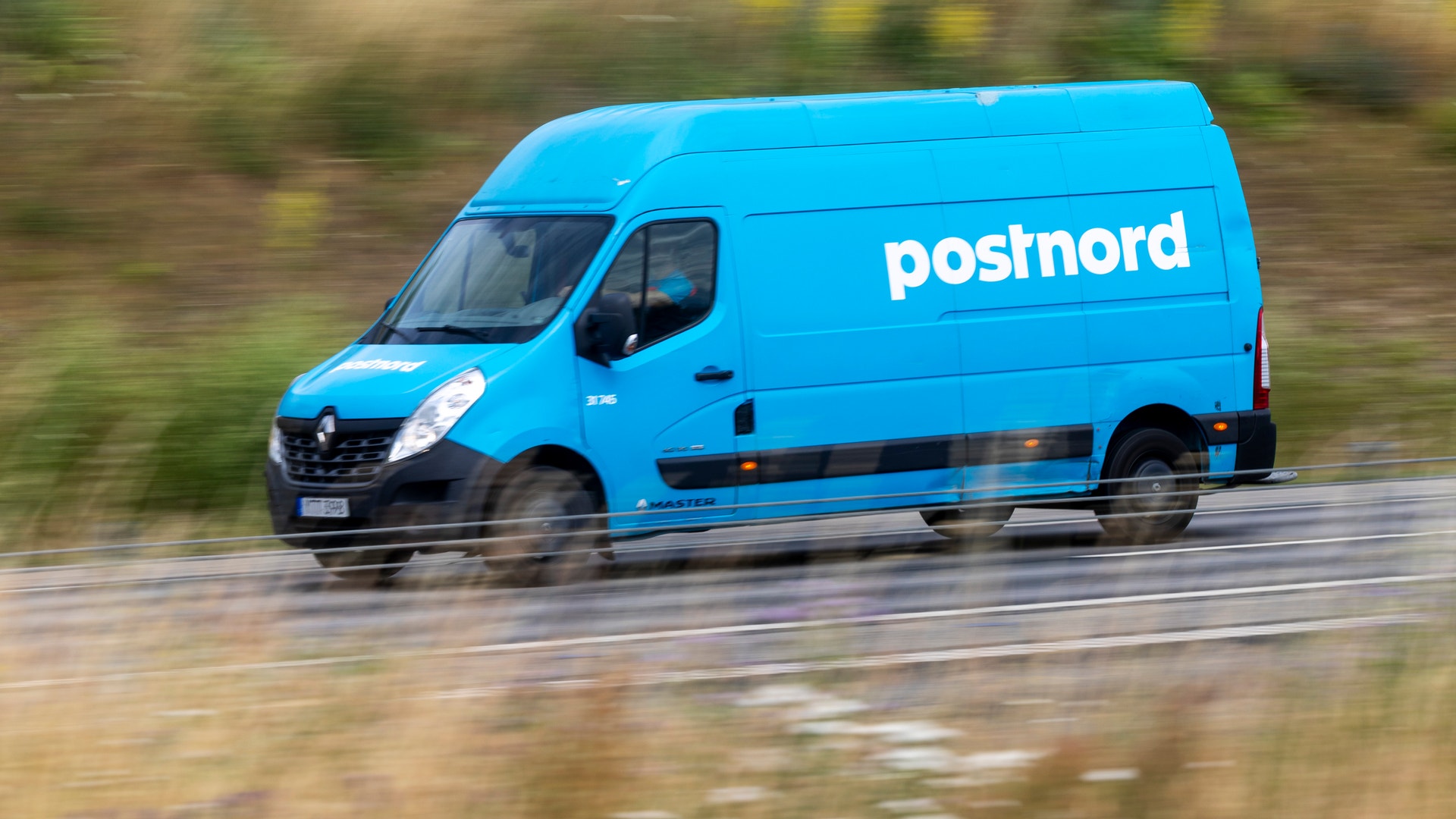 En blå Postnord-skåpbil kör på en väg.