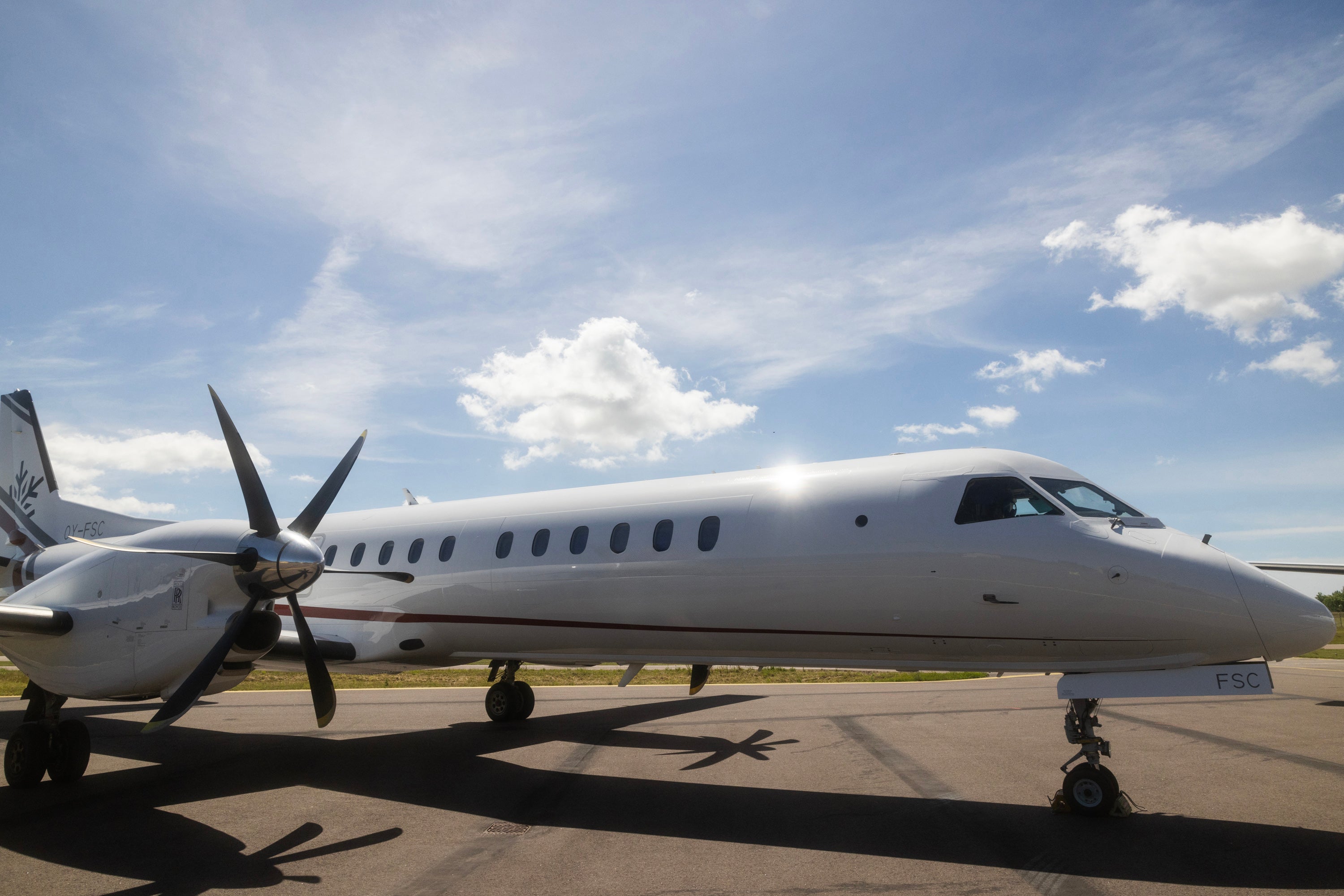 Ett silverfärgat passagerarflygplan med två propellrar parkerat på en landningsbana under blå himmel med vita moln.