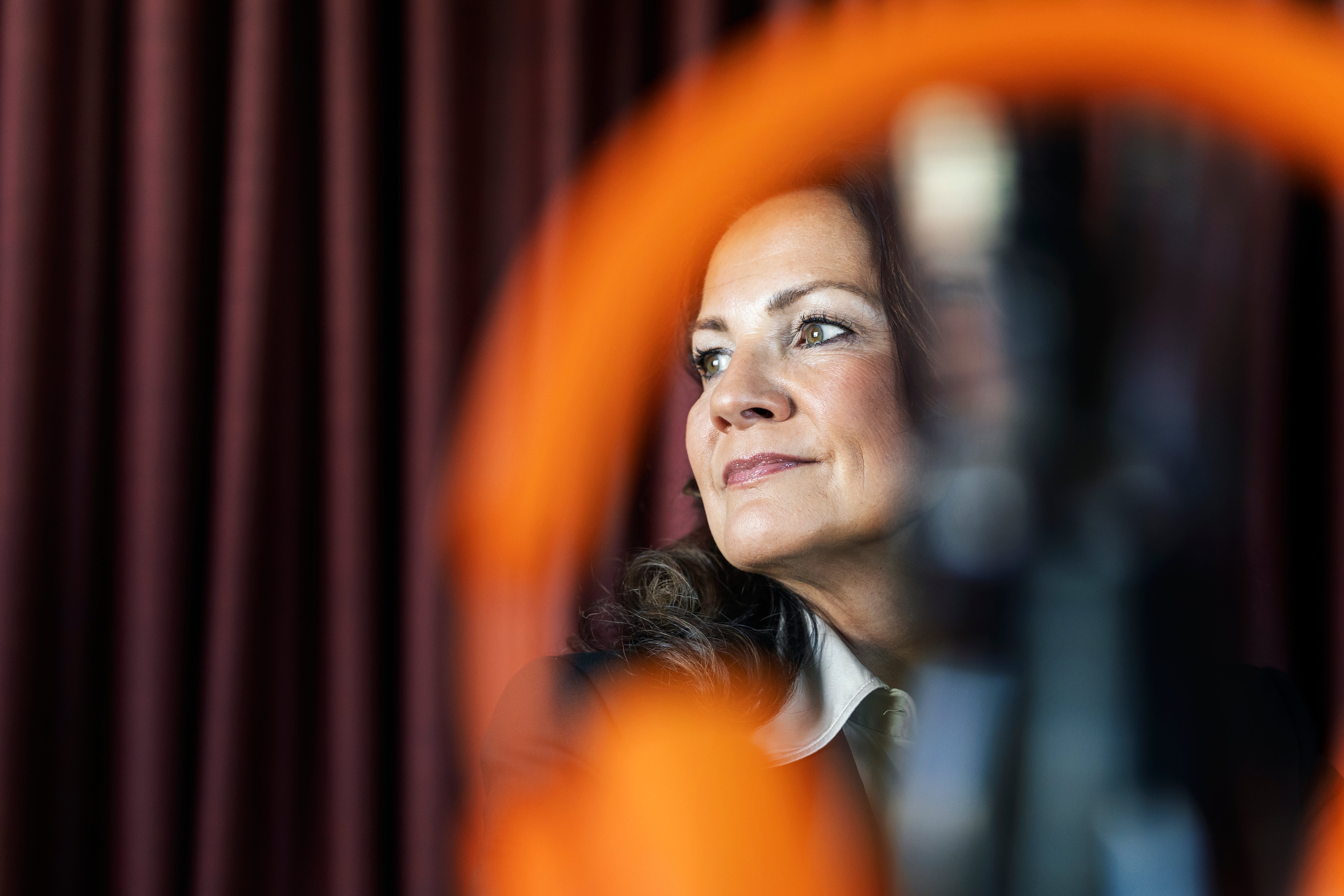 Porträtt av en kvinna som ser ut mot sidan framför en röd gardin. En orange cirkulär form är suddig i förgrunden.