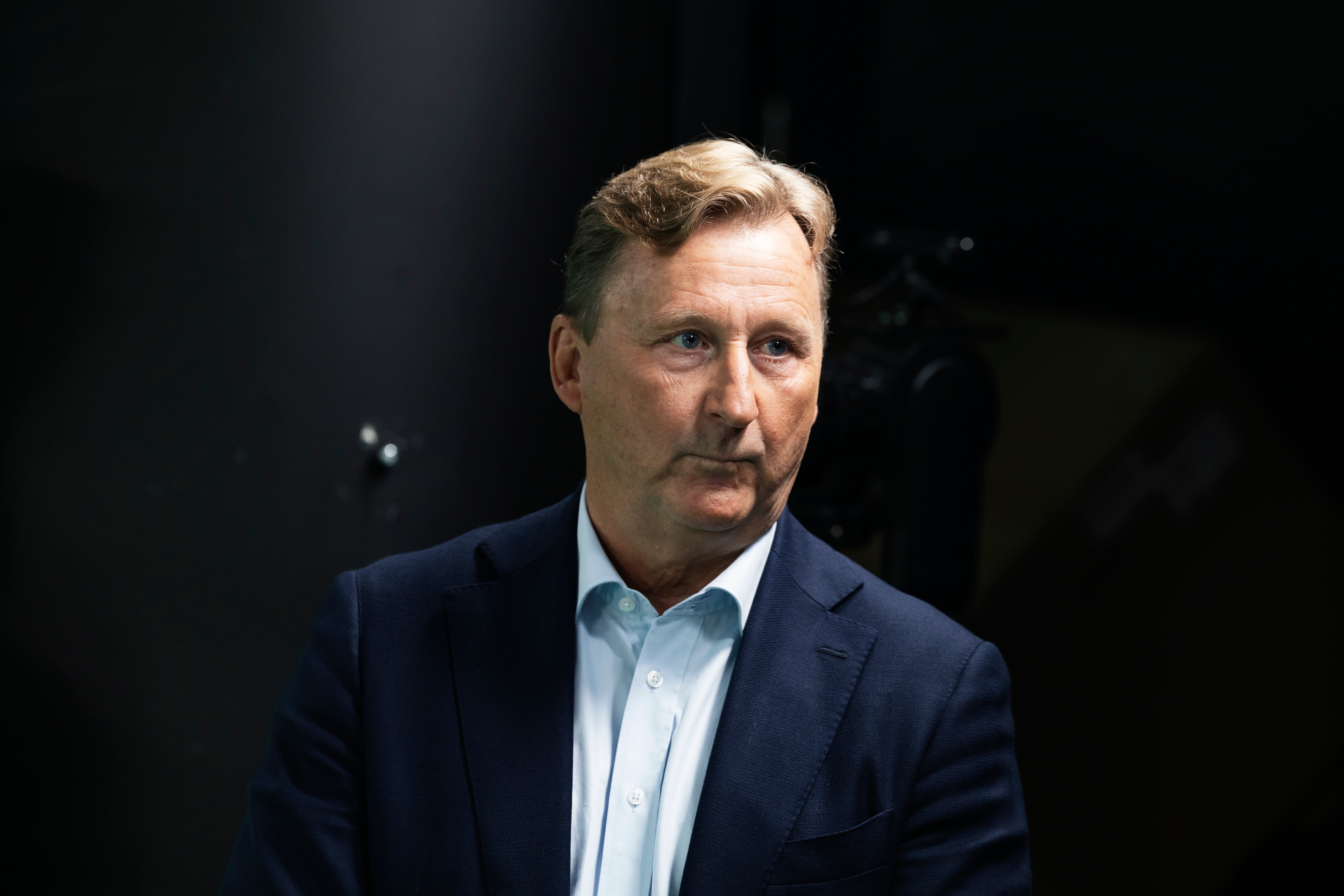Porträtt av en man i mörk kostym och ljus skjorta mot mörk bakgrund.