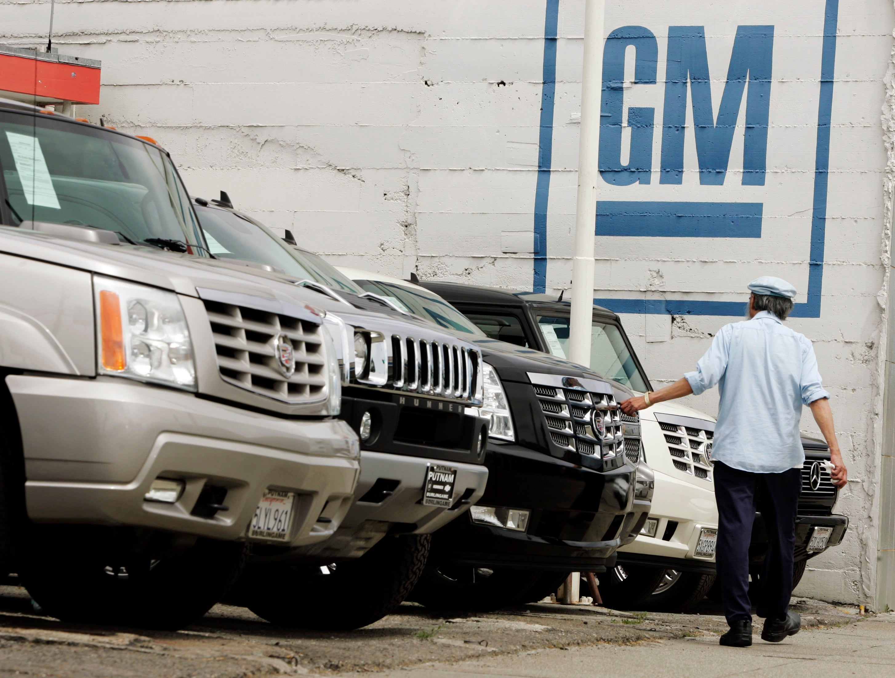 En man går förbi en rad parkerade bilar på en bilplats. På väggen bakom syns General Motors logotyp, GM.