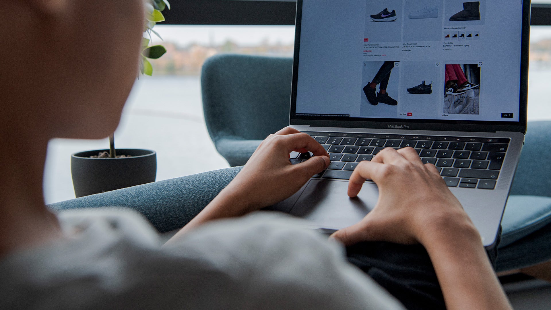 Person som använder en bärbar dator för att handla online. Skärmen visar en e-handelswebbplats med skor och kläder.