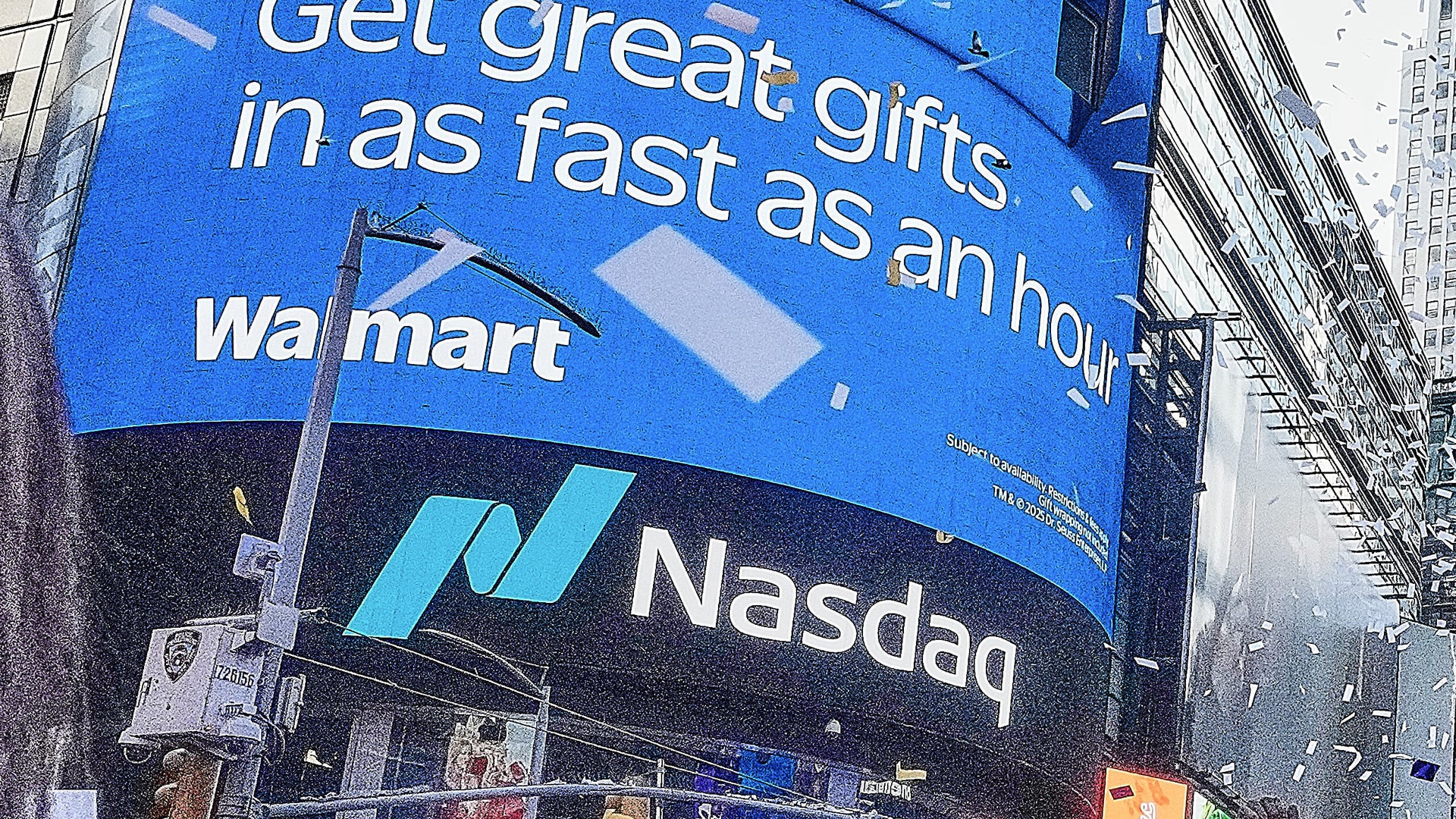 En stor digital reklamskärm på en byggnad visar Walmart och Nasdaq logotyper med text om gåvor.