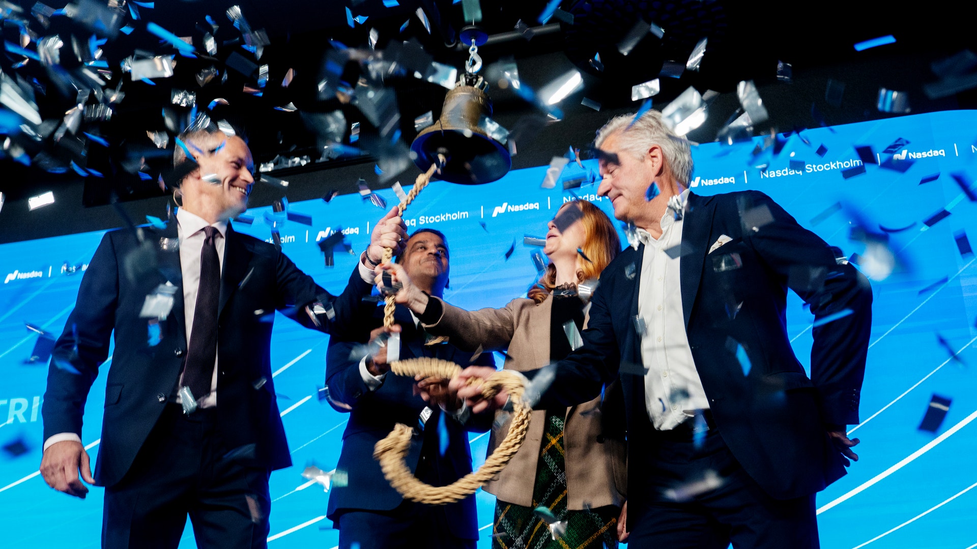Personer i kostym ringer i klocka på en scen medan konfetti faller, vid en börsnotering på Nasdaq Stockholm.